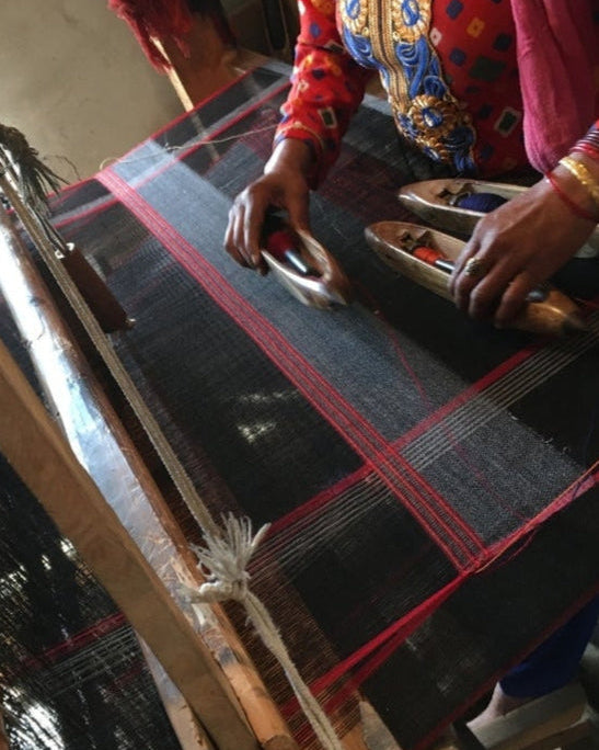 Person operating a traditional loom with colorful patterns on clothing.