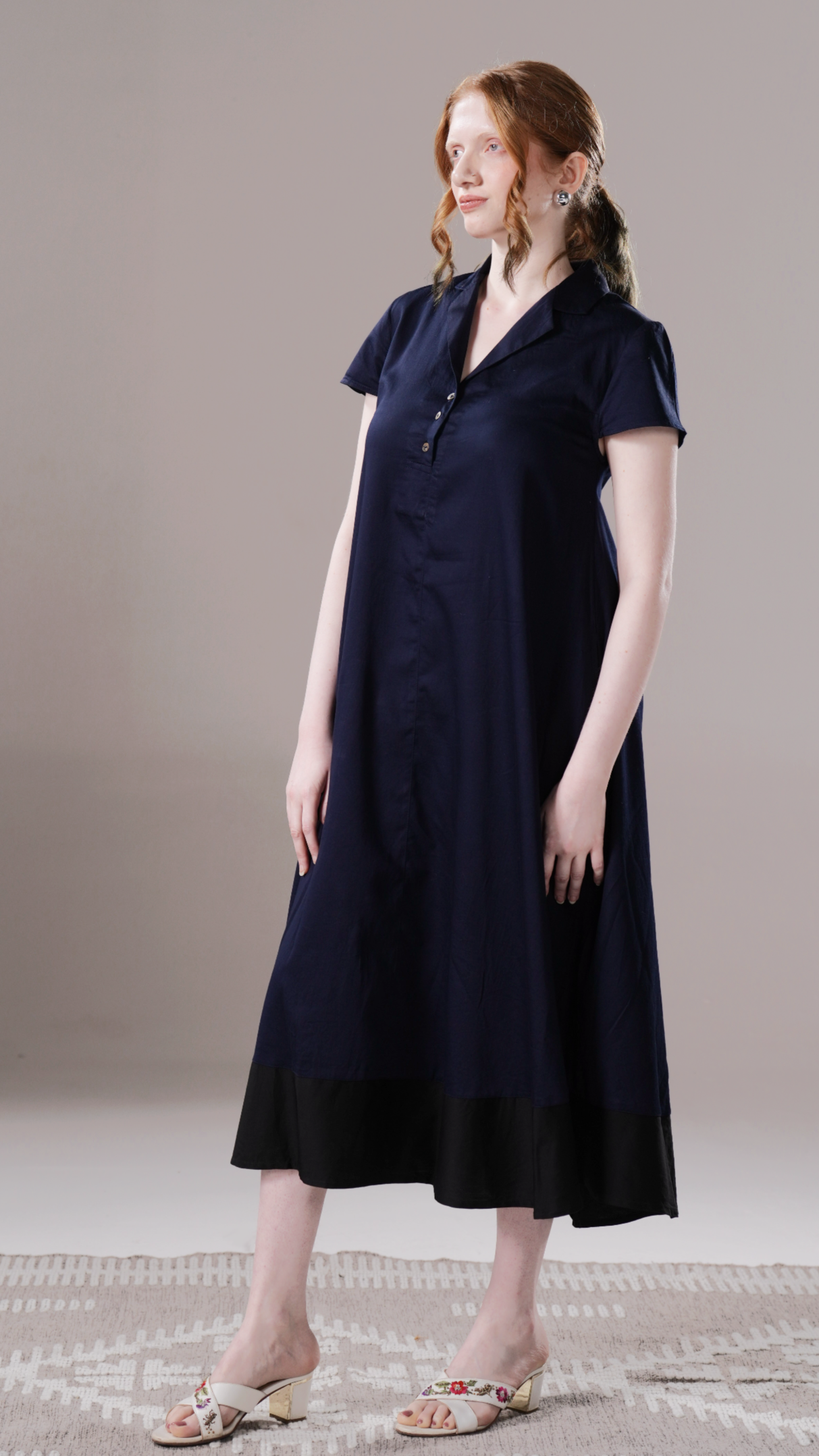 Woman wearing a navy dress standing against a plain background