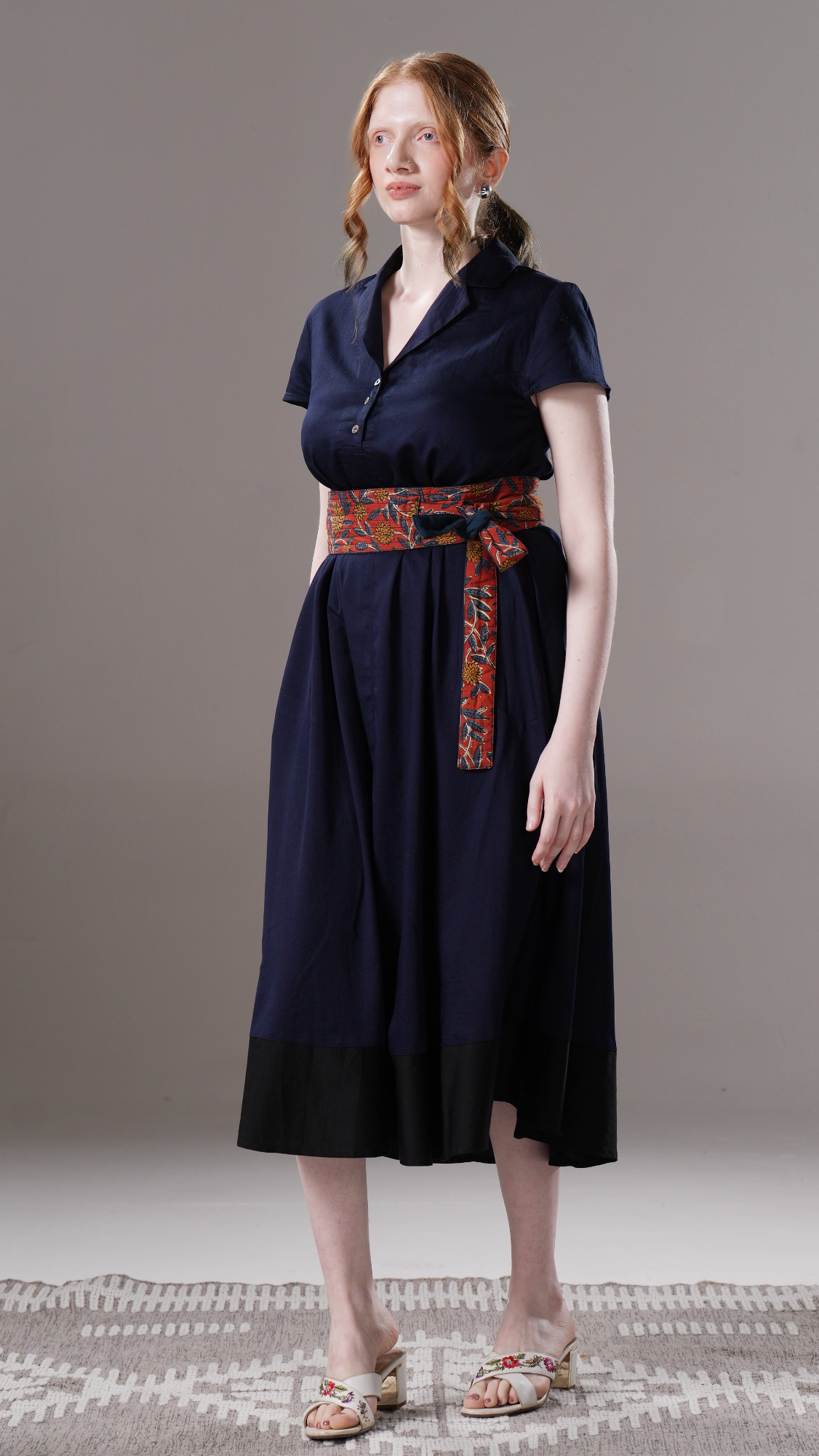 Woman wearing a navy dress with a patterned belt against a neutral background