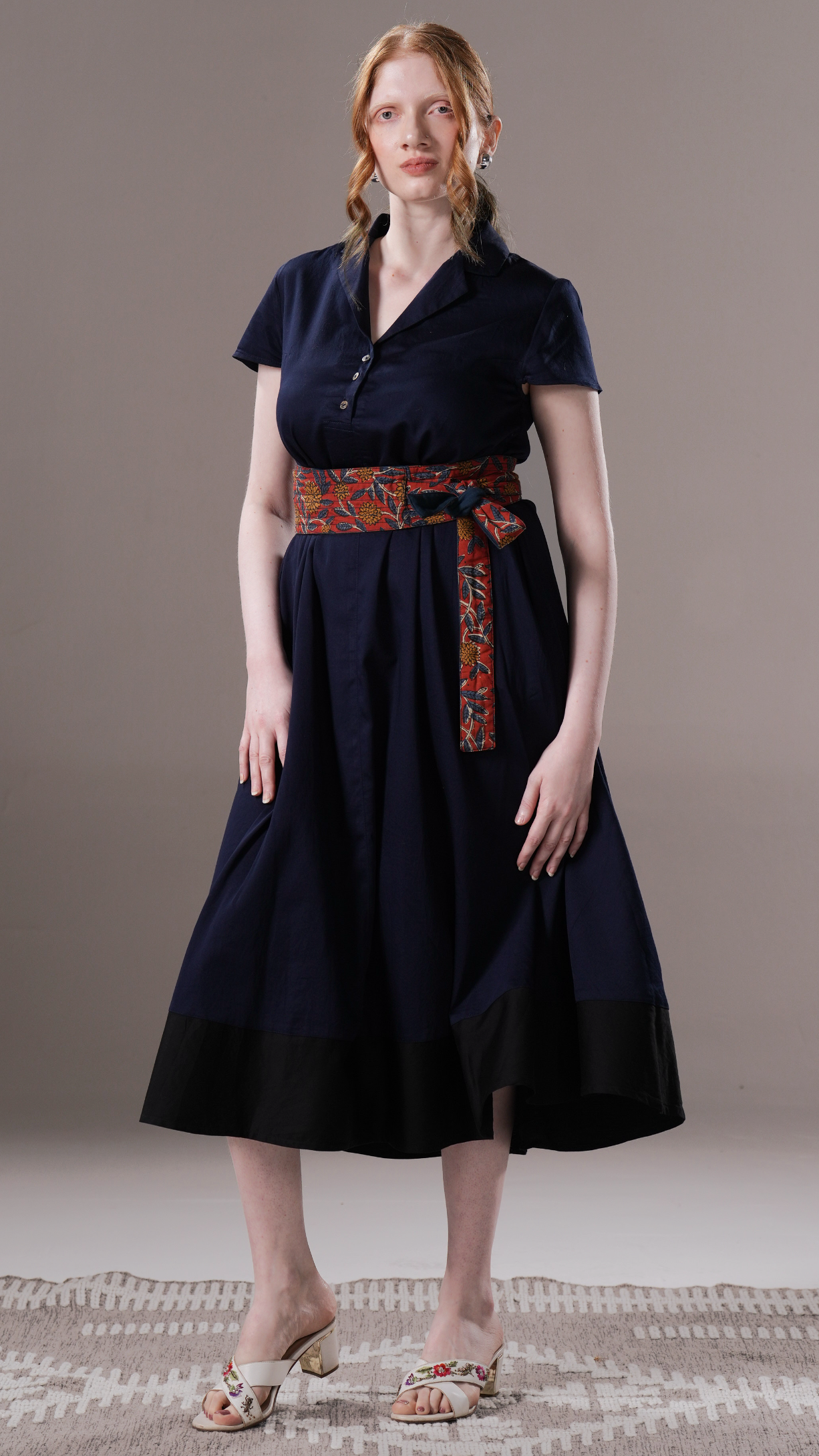 Woman wearing a navy dress with a patterned belt on a neutral background