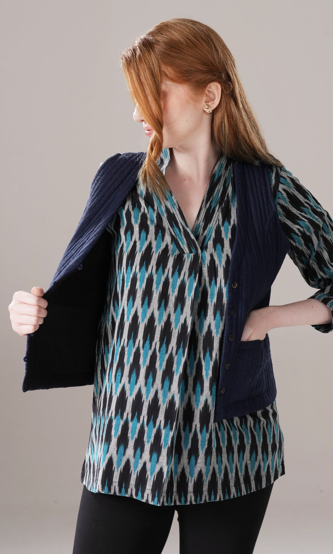 Woman wearing a patterned shirt and navy vest against a plain background
