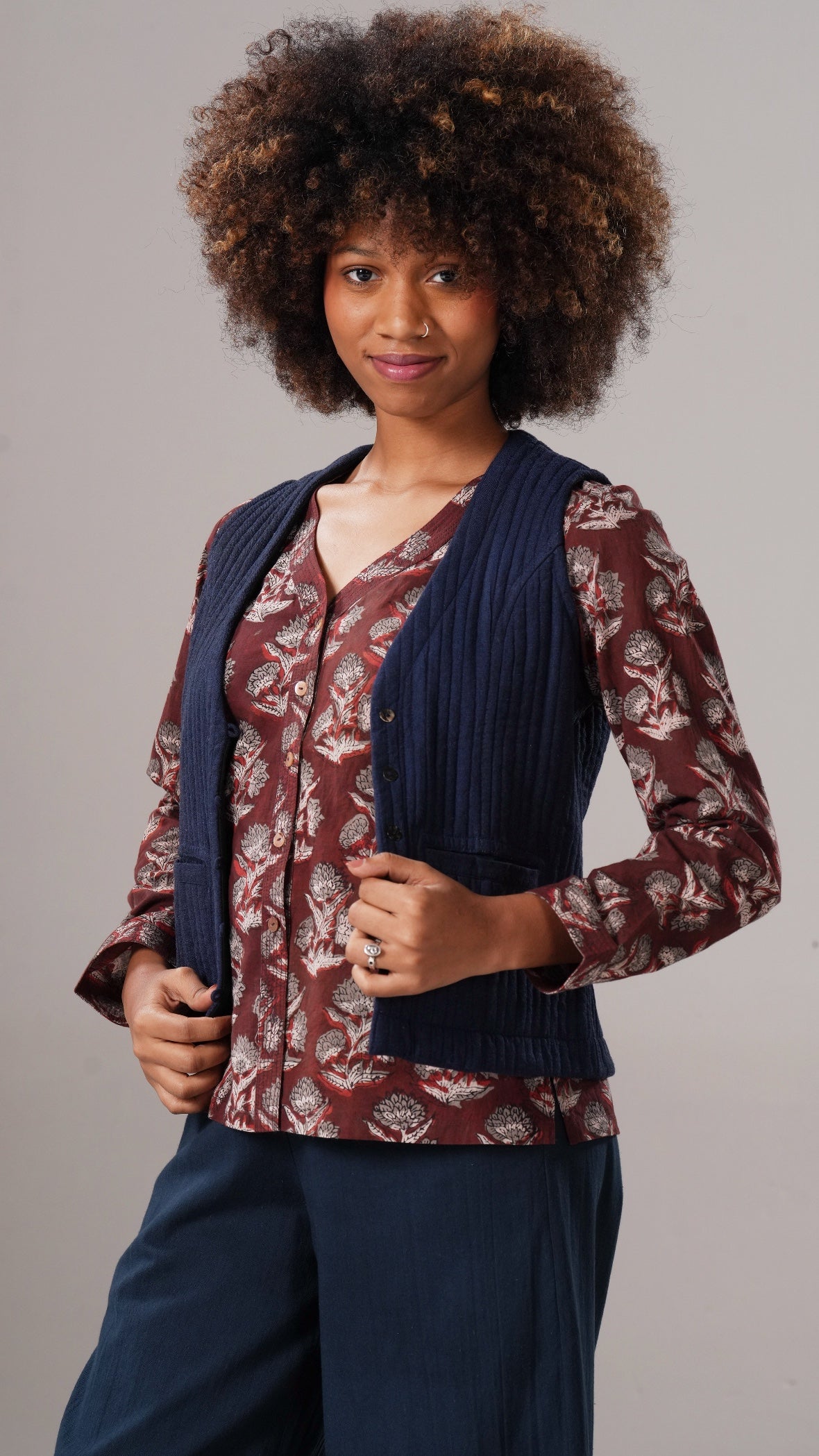 Woman wearing a patterned blouse with a navy cardigan against a gray background
