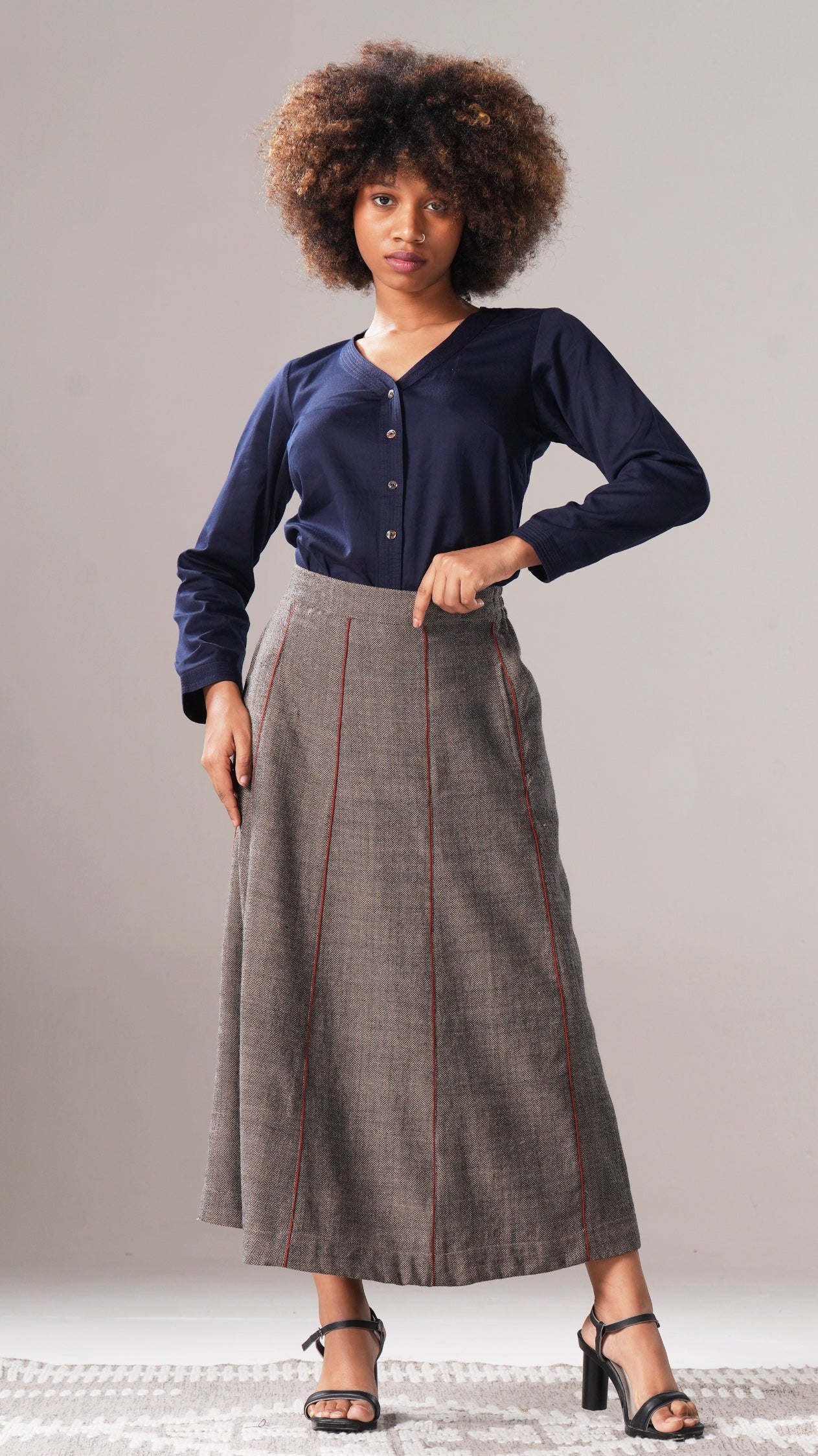 Woman wearing a navy shirt and gray skirt against a plain background