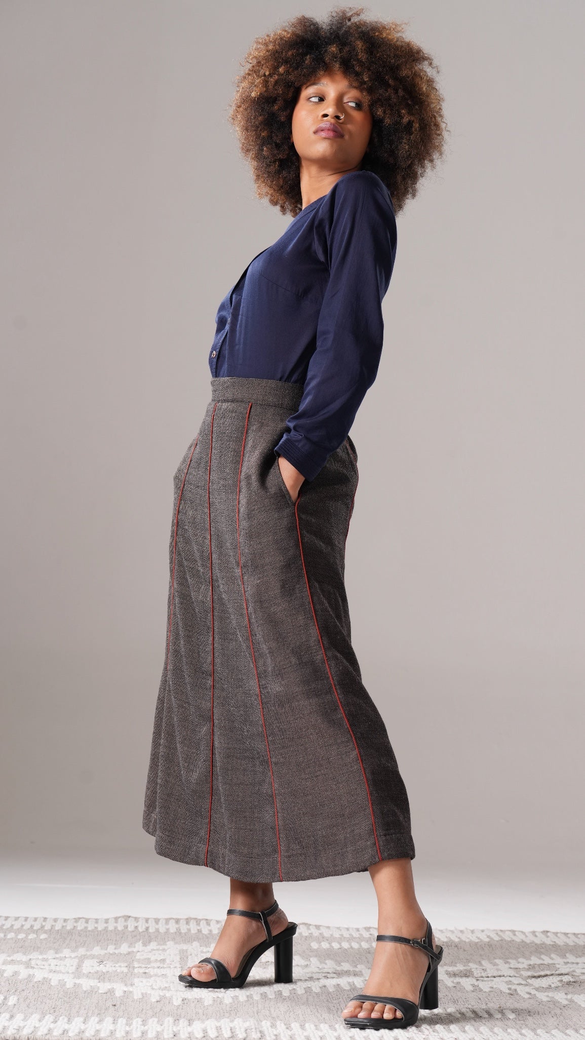 Woman wearing a blue blouse and gray skirt with red stitching on a neutral background