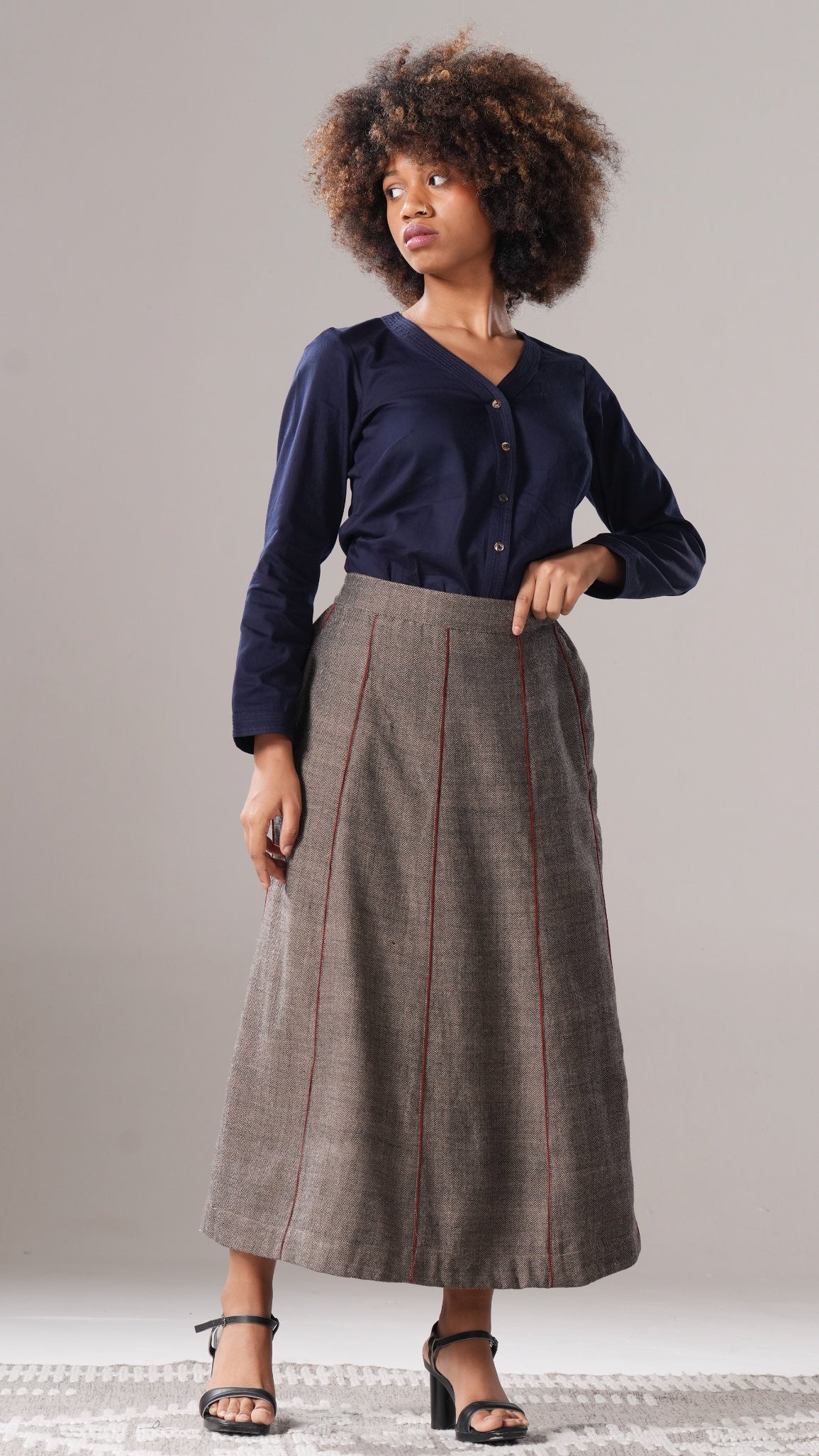 Woman wearing a navy shirt and long plaid skirt against a plain background