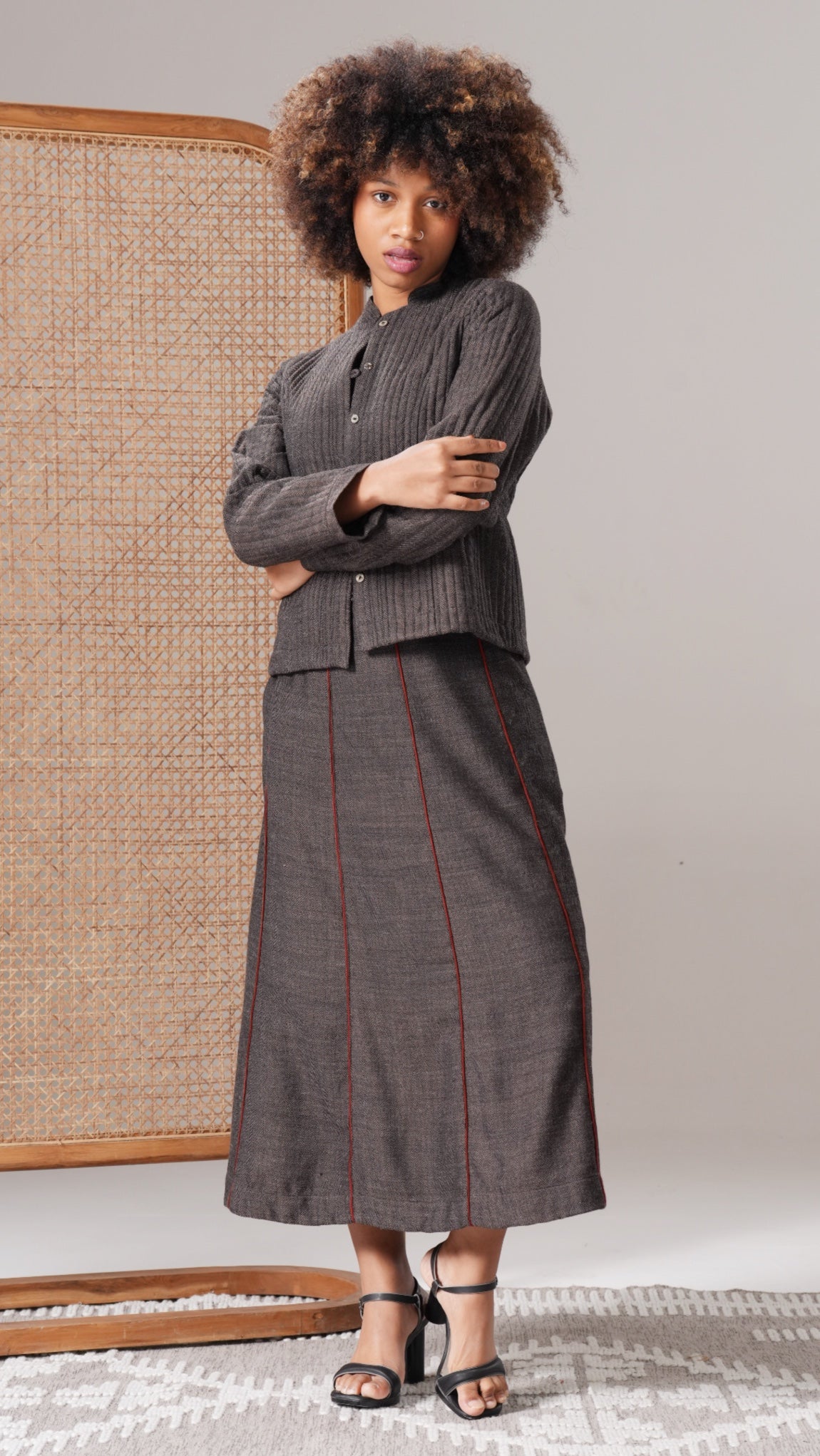 Woman wearing a gray suit with a patterned skirt standing against a neutral background