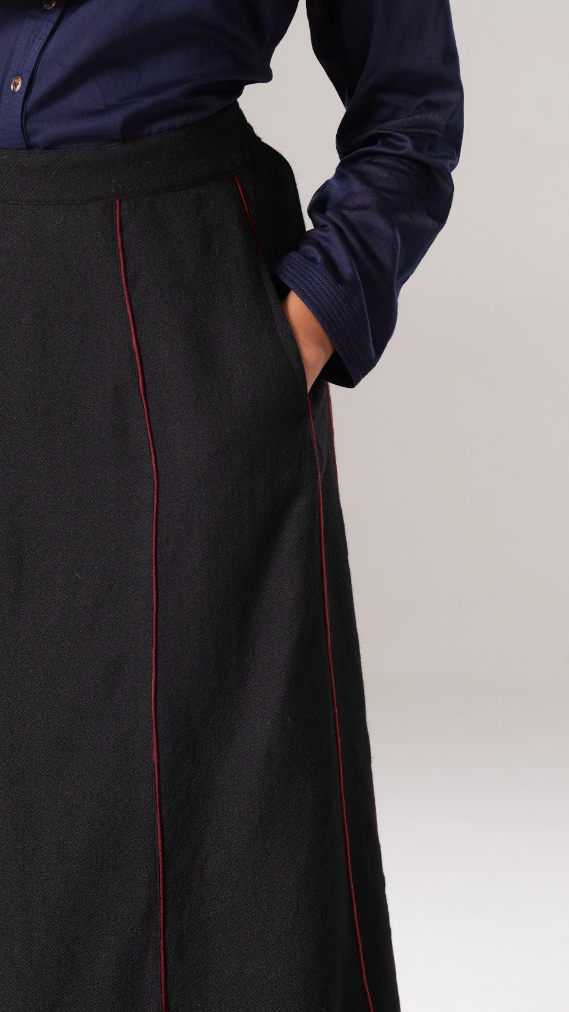 Person wearing a dark blue shirt and black skirt with red piping on a light gray background