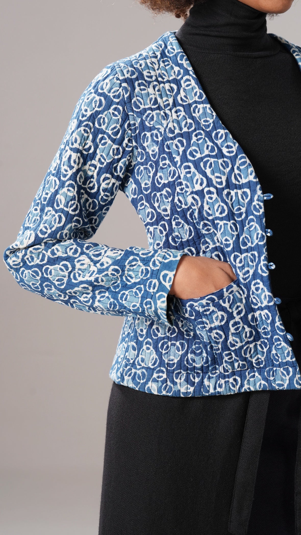 Blue patterned jacket over a black turtleneck and skirt on a neutral background