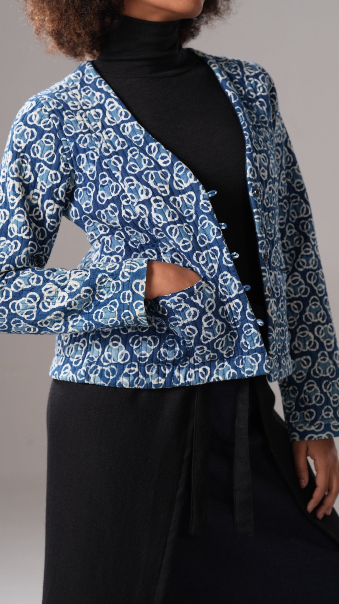 Person wearing a blue patterned jacket over a black outfit on a plain background