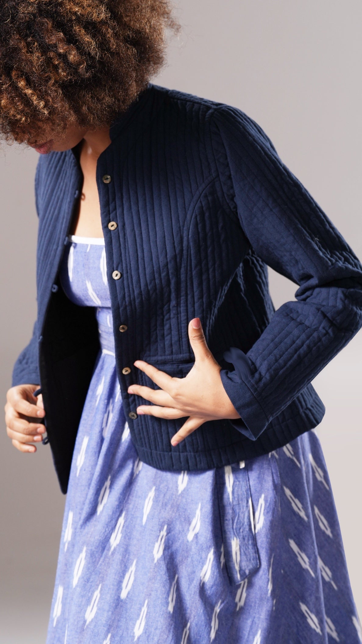Woman wearing a blue ribbed knit cardigan over a patterned dress against a neutral background