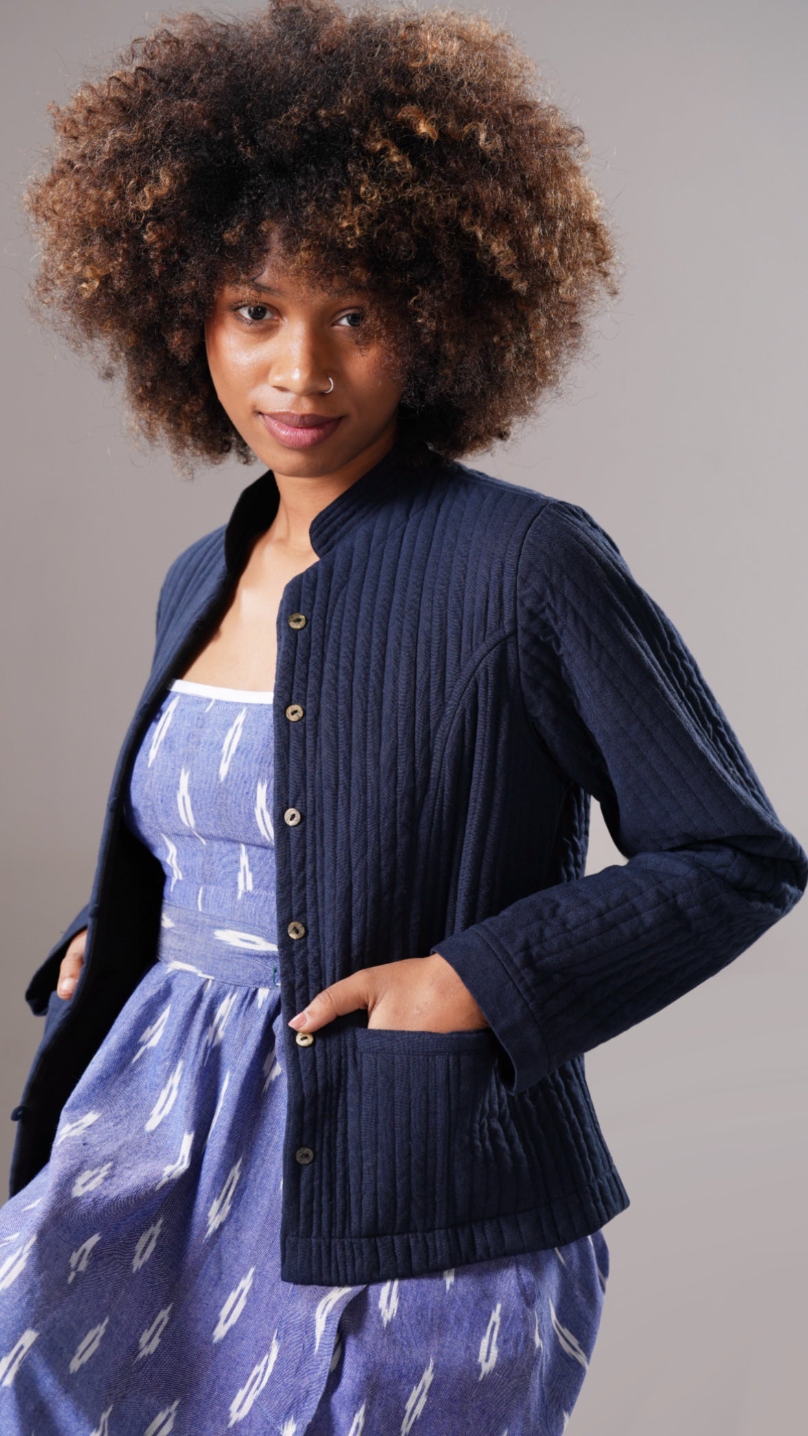 Woman wearing a navy cardigan over a blue dress with feather pattern on a gray background