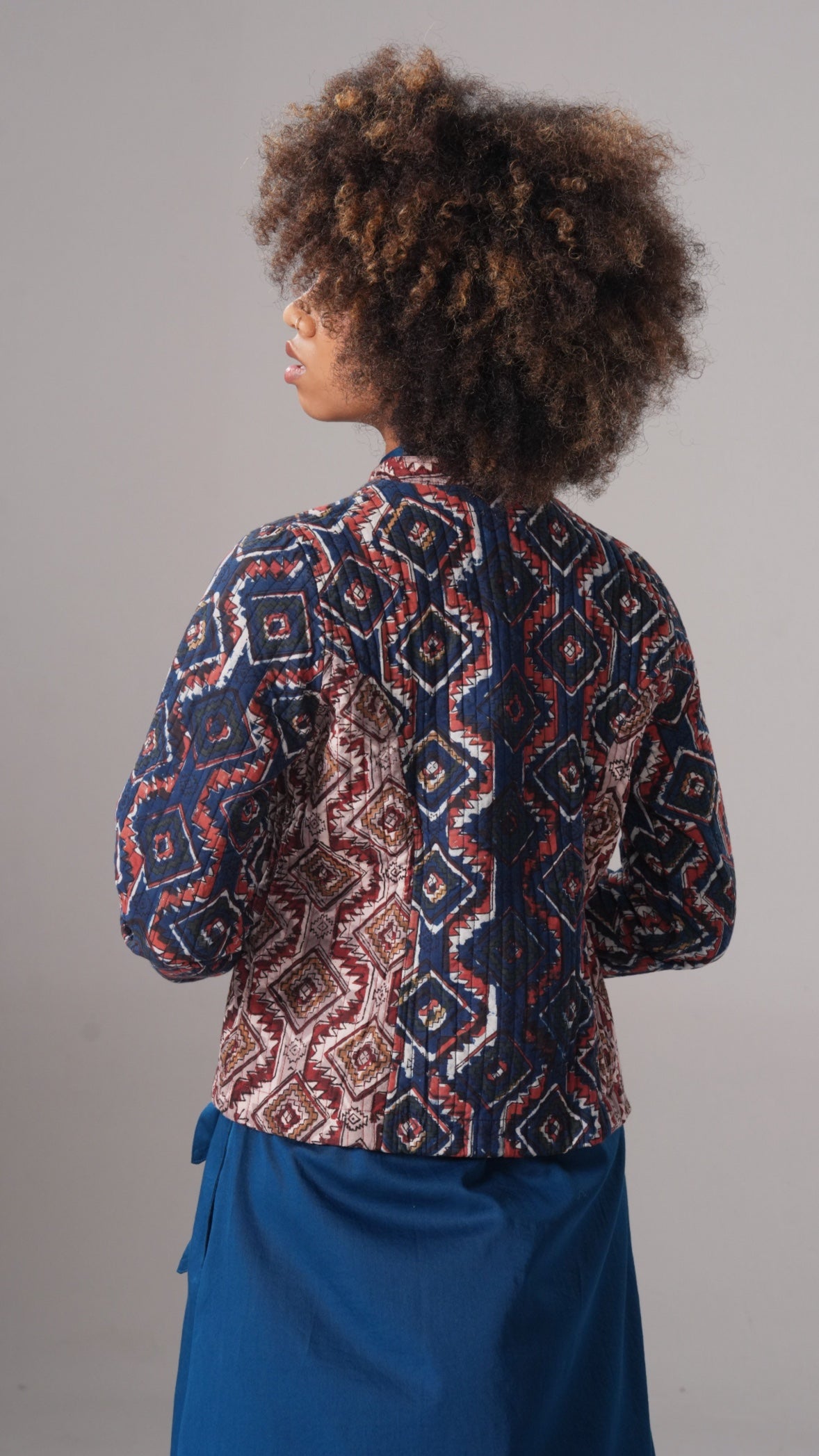 Person wearing a patterned jacket and blue pants against a gray background