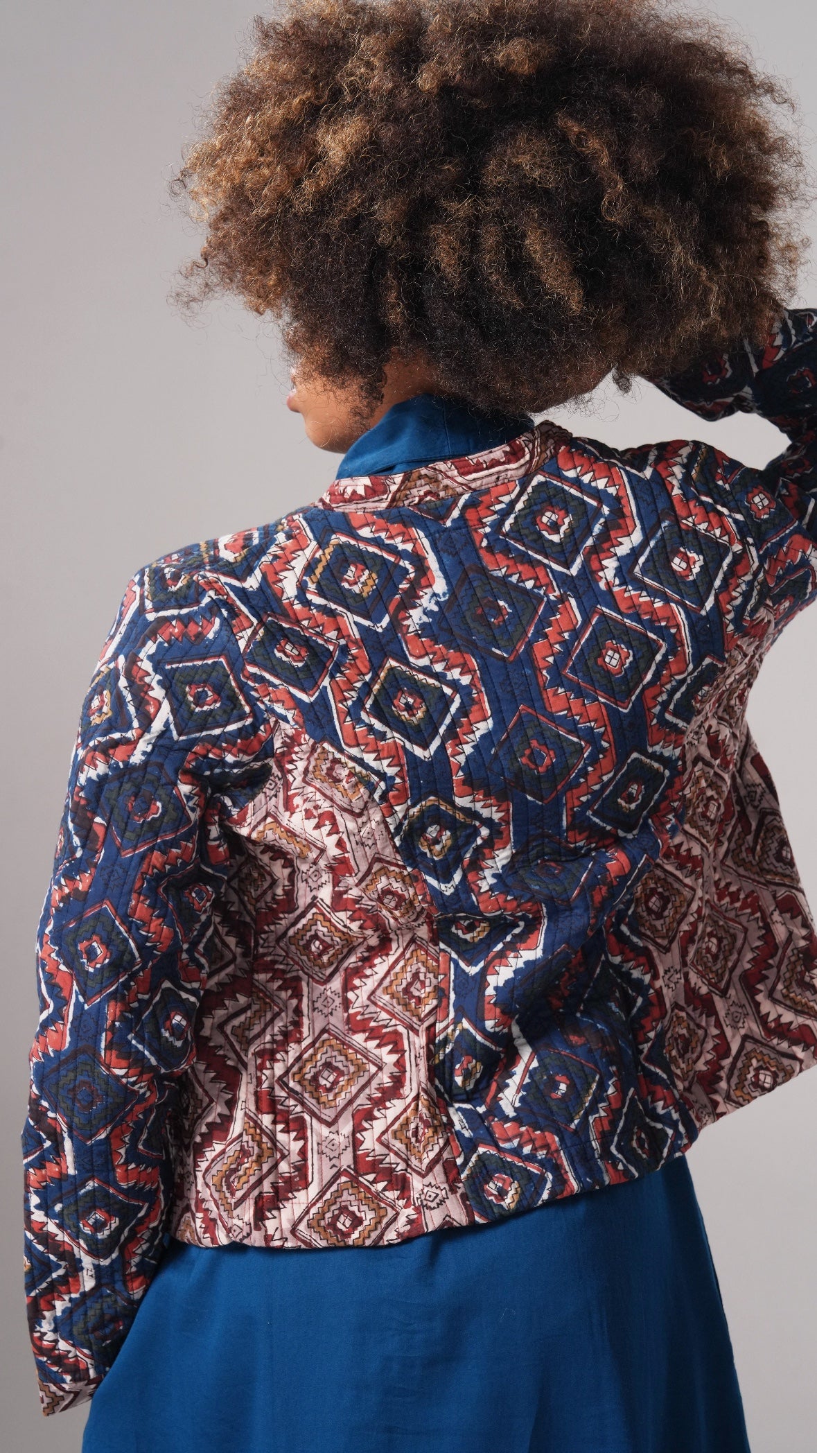 Person wearing a patterned jacket over a blue outfit on a gray background