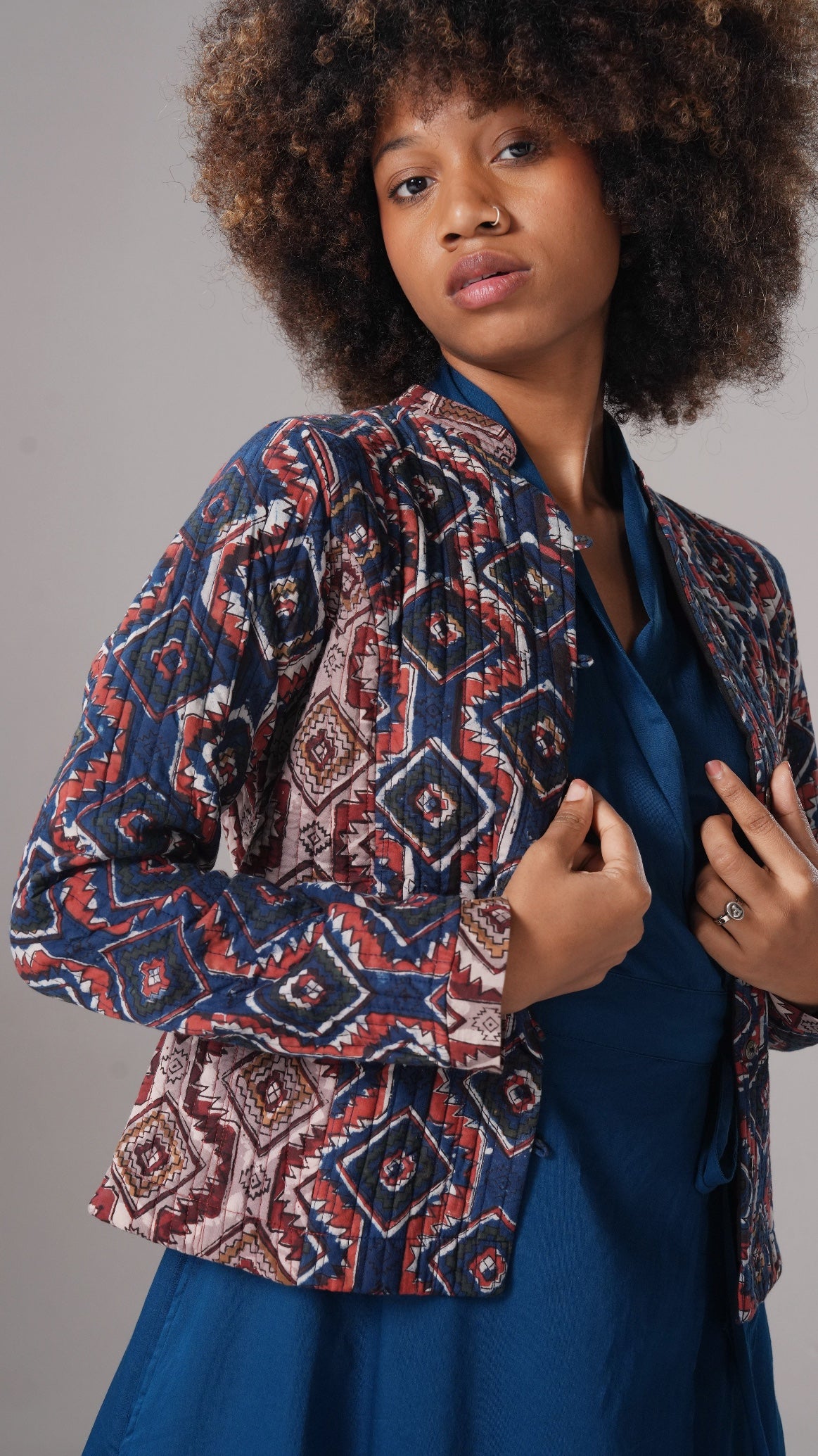 Woman wearing a patterned jacket over a blue dress against a gray background