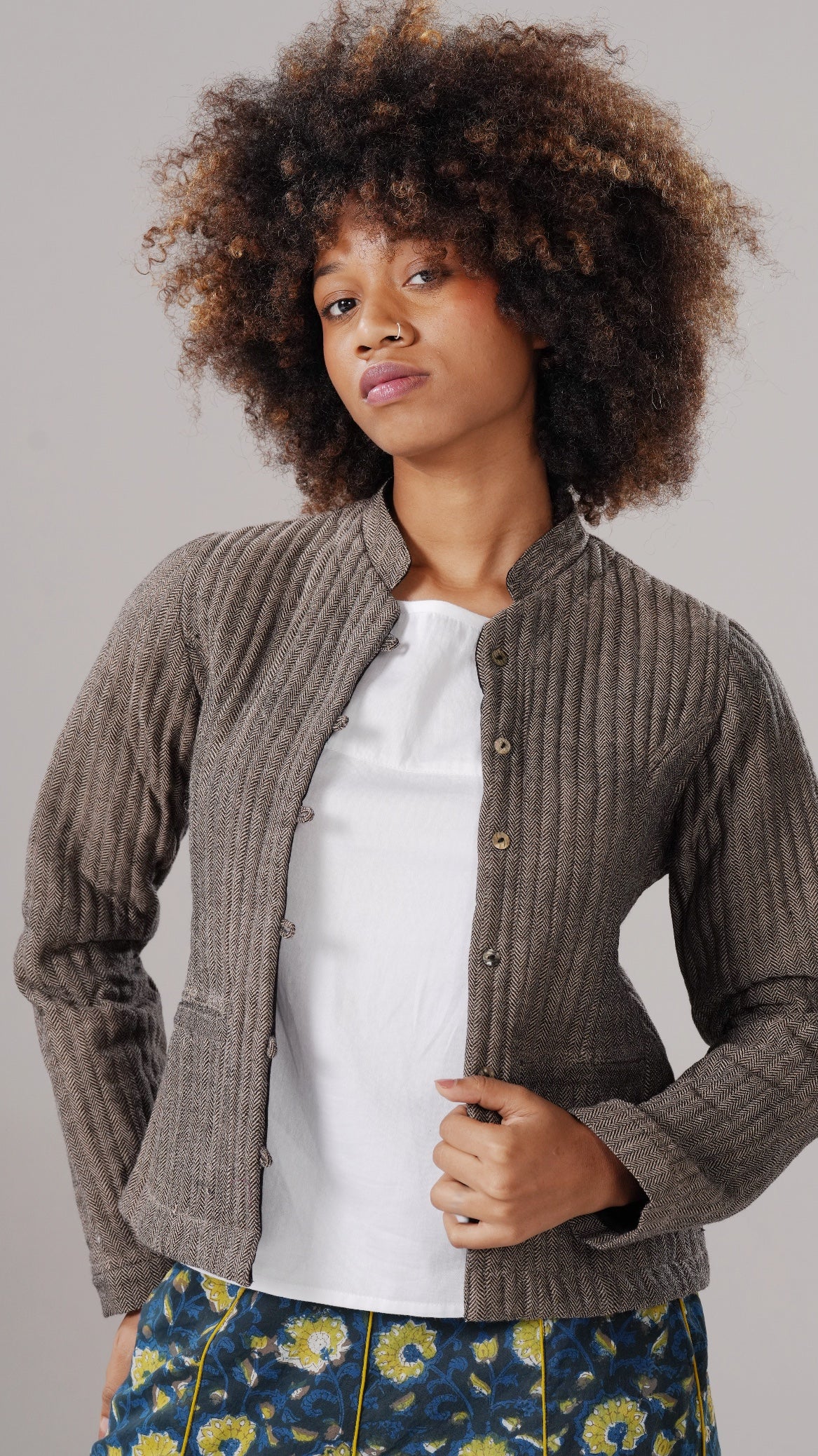 Woman wearing a brown ribbed cardigan over a white shirt with a gray background