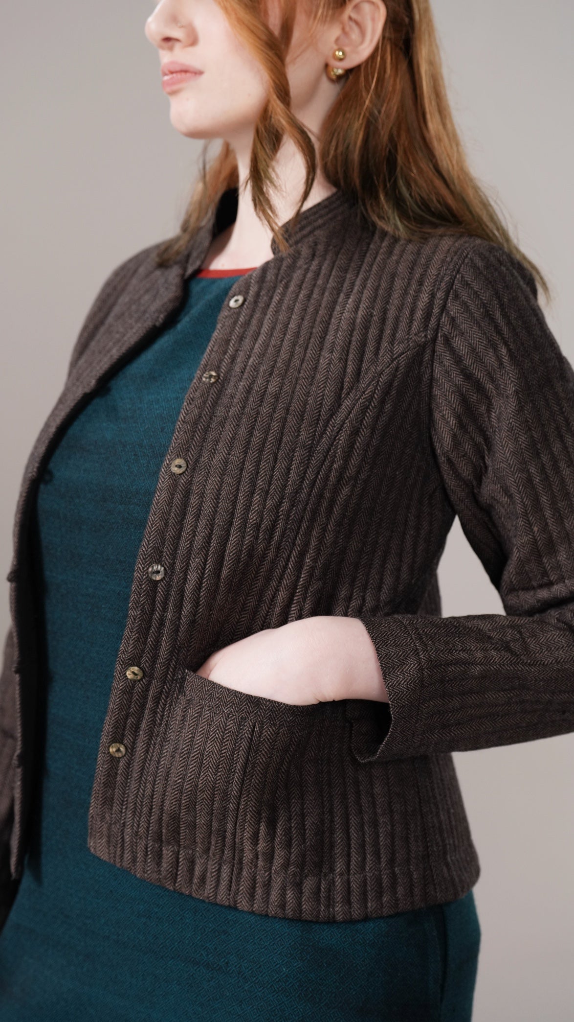Woman wearing a brown ribbed cardigan over a teal dress against a neutral background
