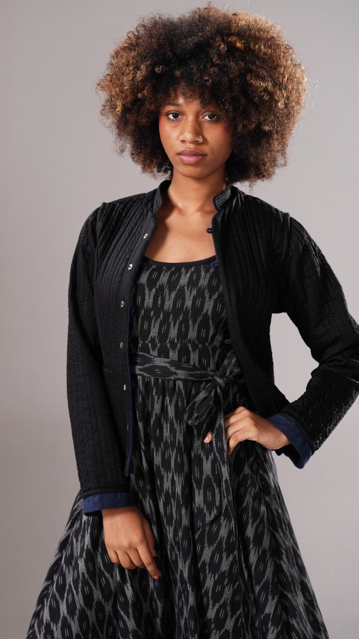 Woman wearing a black cardigan over a patterned dress against a gray background