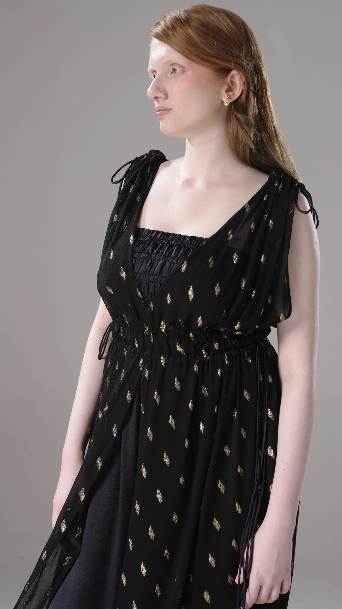 Woman wearing a black dress with gold patterns against a gray background