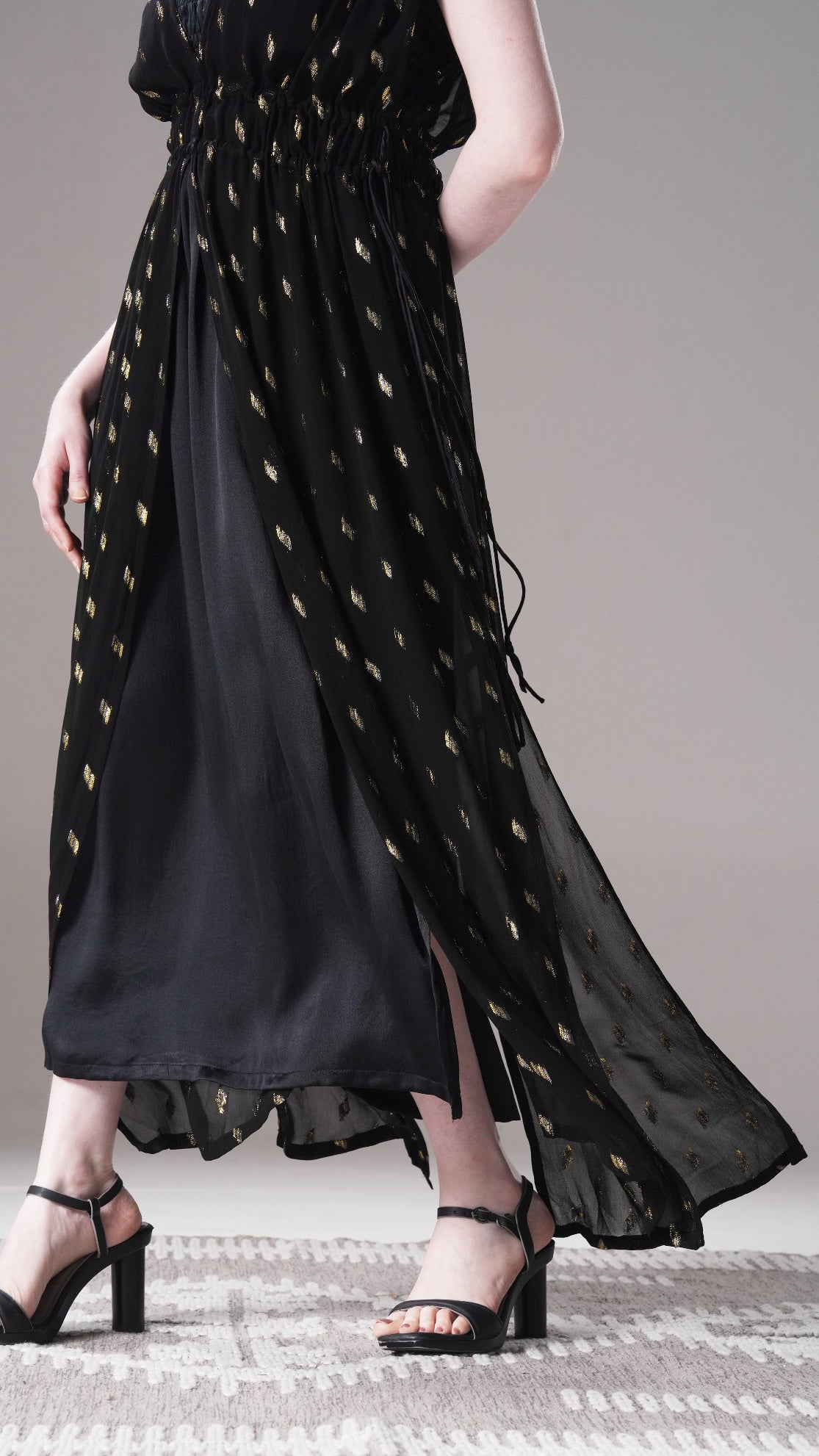 Black dress with gold patterns worn by a person on a neutral background