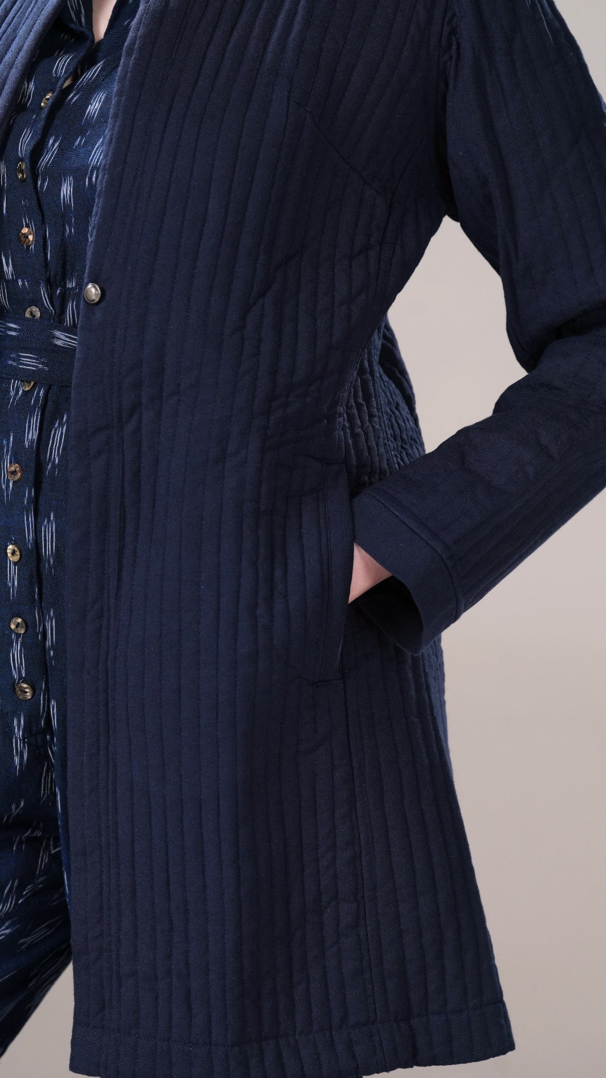 Navy blue ribbed coat worn over a patterned shirt on a neutral background
