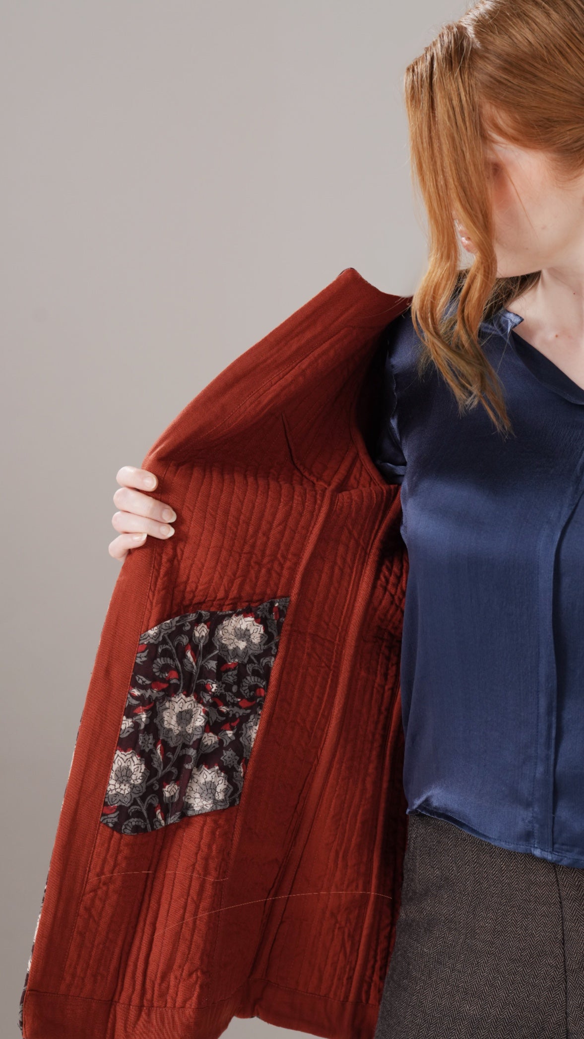 Person wearing a red jacket with a floral pocket on a plain background