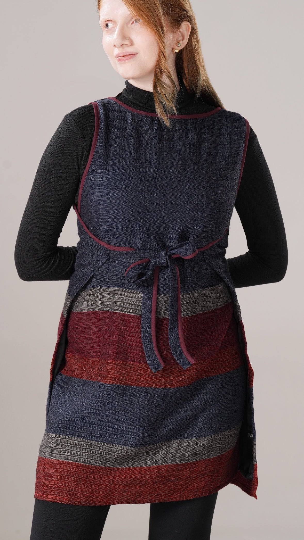 Woman wearing a striped dress with a dark blue and red pattern on a plain background