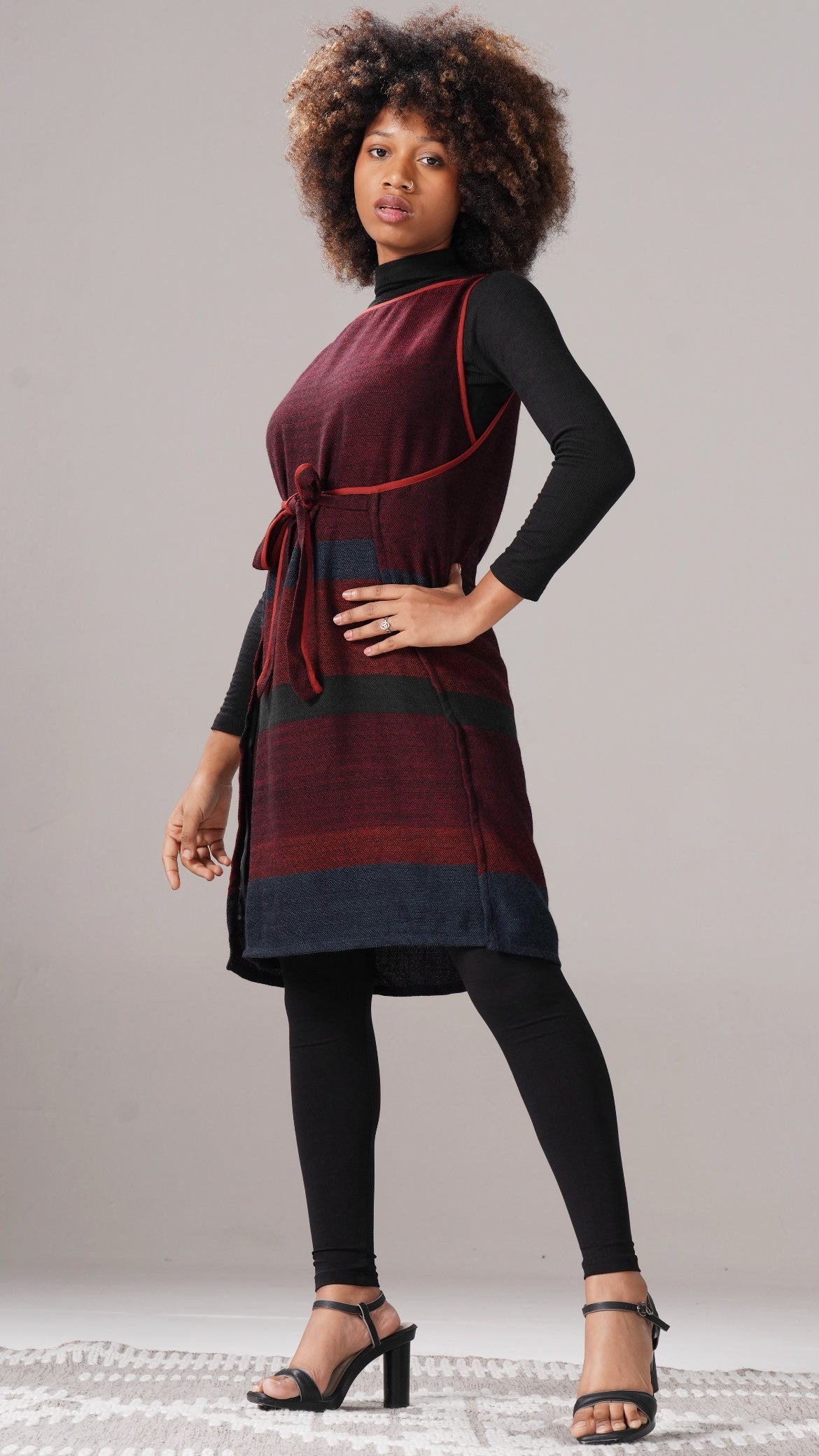 Woman wearing a maroon and black dress with a belt on a gray background