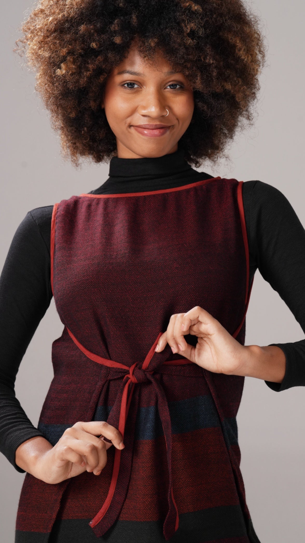 Woman wearing a burgundy vest with a red tie against a gray background