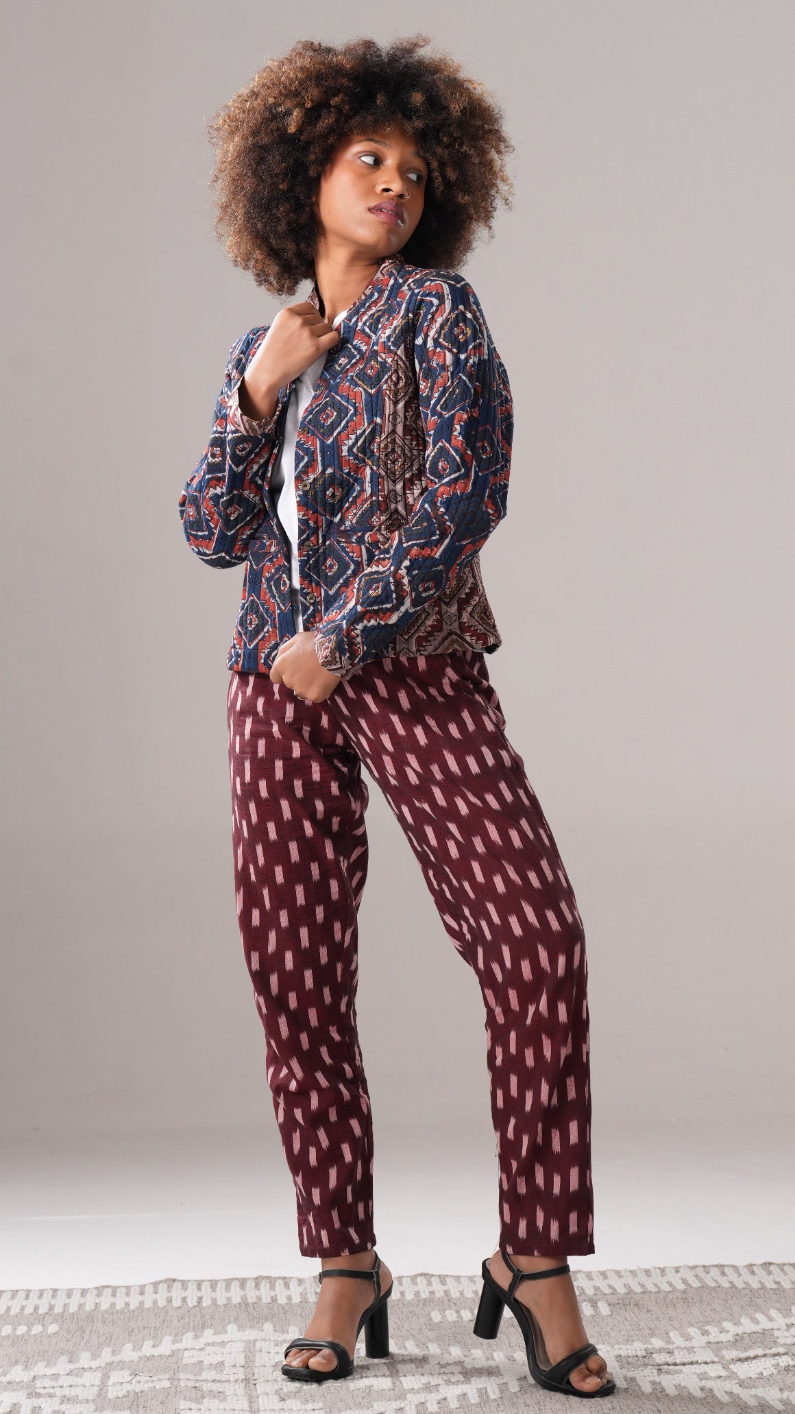 Woman wearing a patterned outfit with a jacket and pants on a plain background
