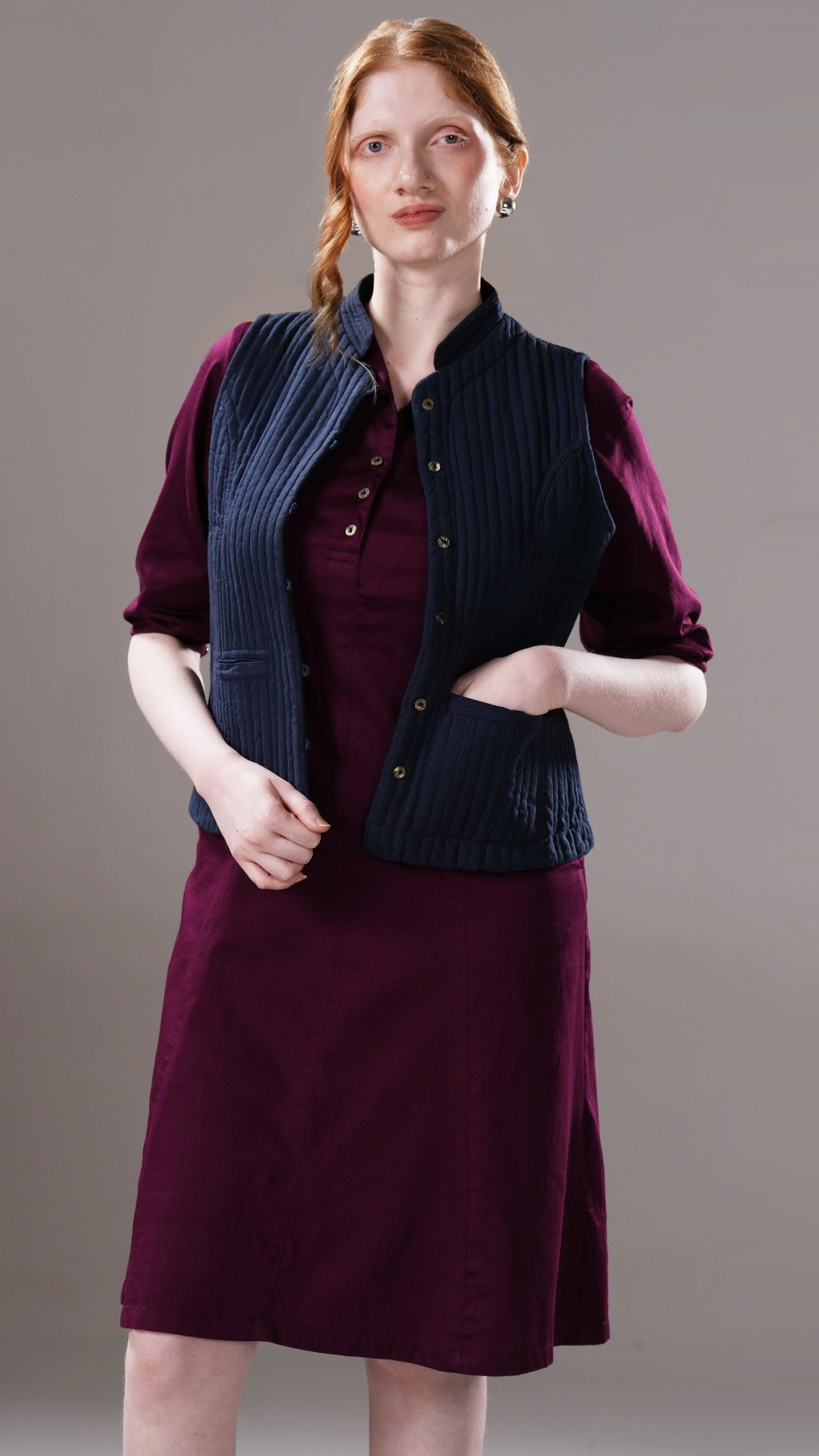 Woman wearing a dark vest over a purple dress against a gray background