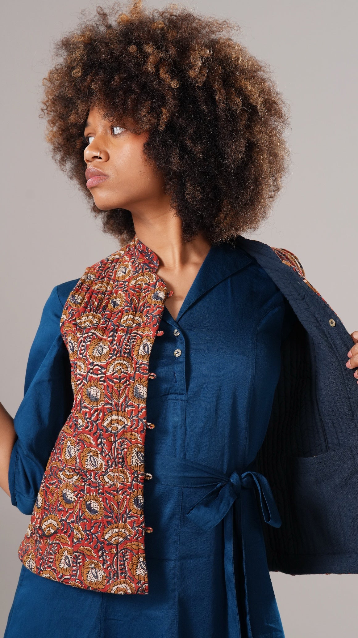 Woman wearing a blue outfit with a patterned scarf against a gray background