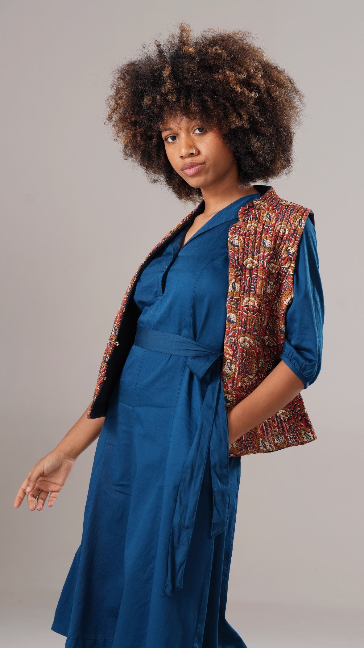 Woman wearing a blue dress with a patterned vest against a gray background