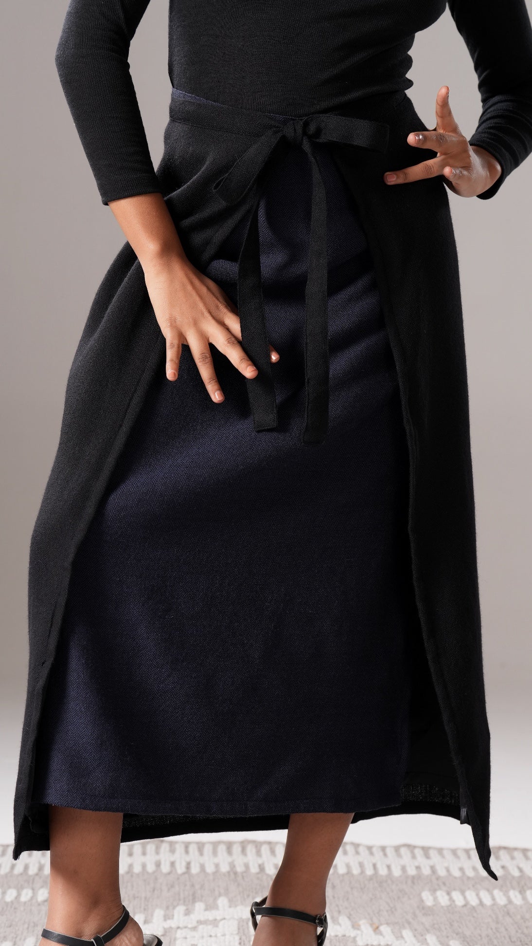 Person wearing a black dress with a belt on a neutral background
