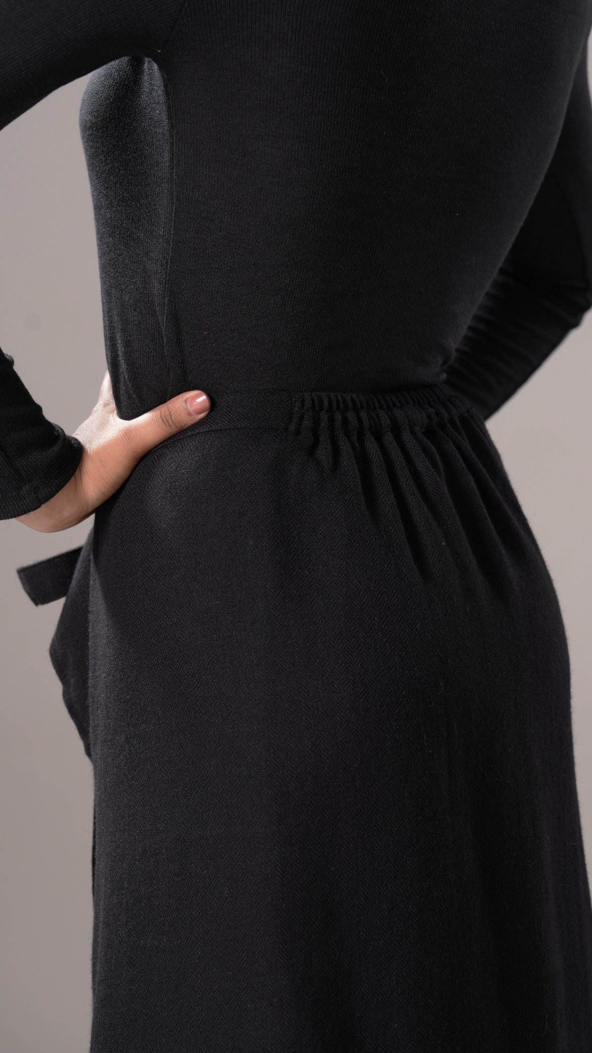 Black dress with long sleeves and a fitted waist on a gray background