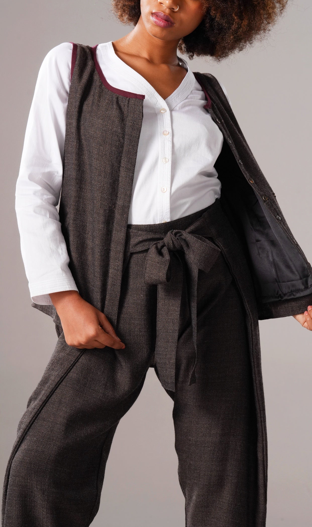 Person wearing a white shirt, dark vest, and wide-leg pants against a gray background