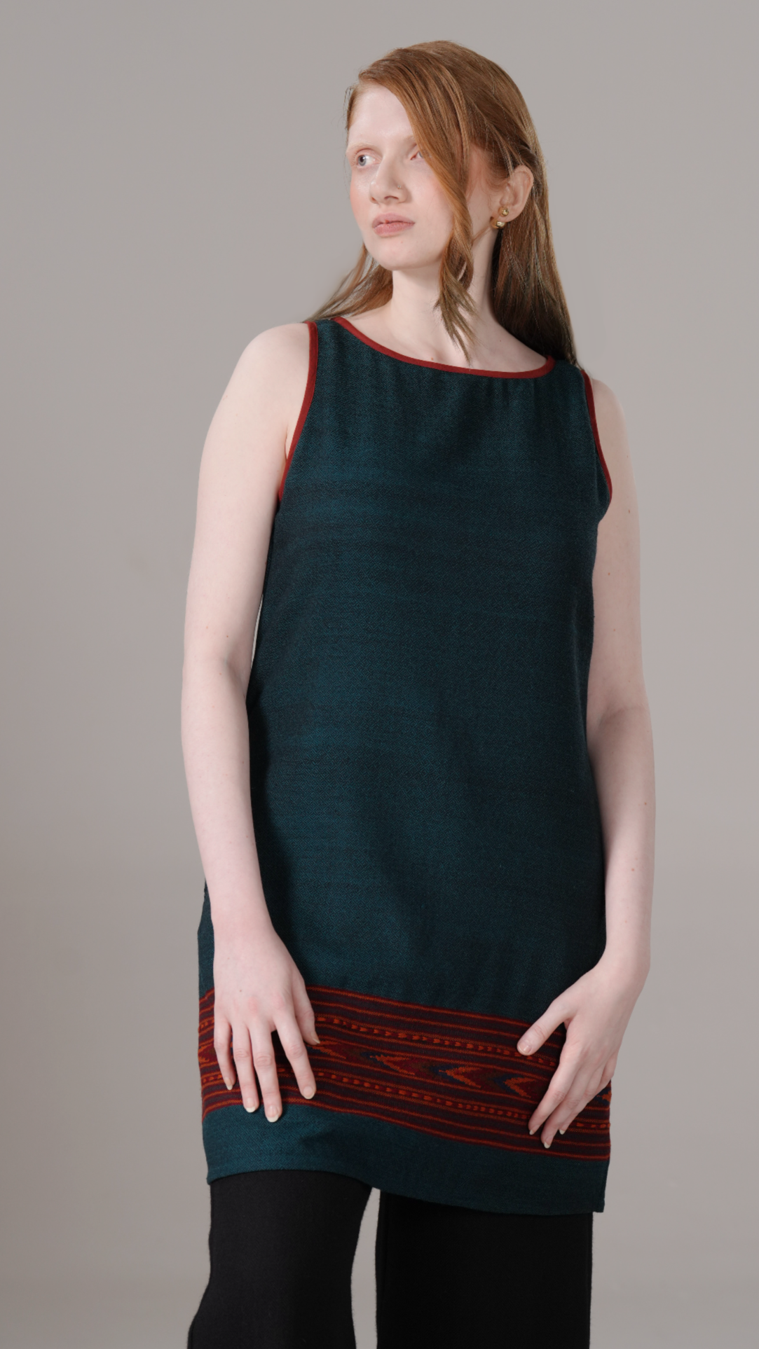 Woman wearing a dark green sleeveless dress with red trim on a gray background
