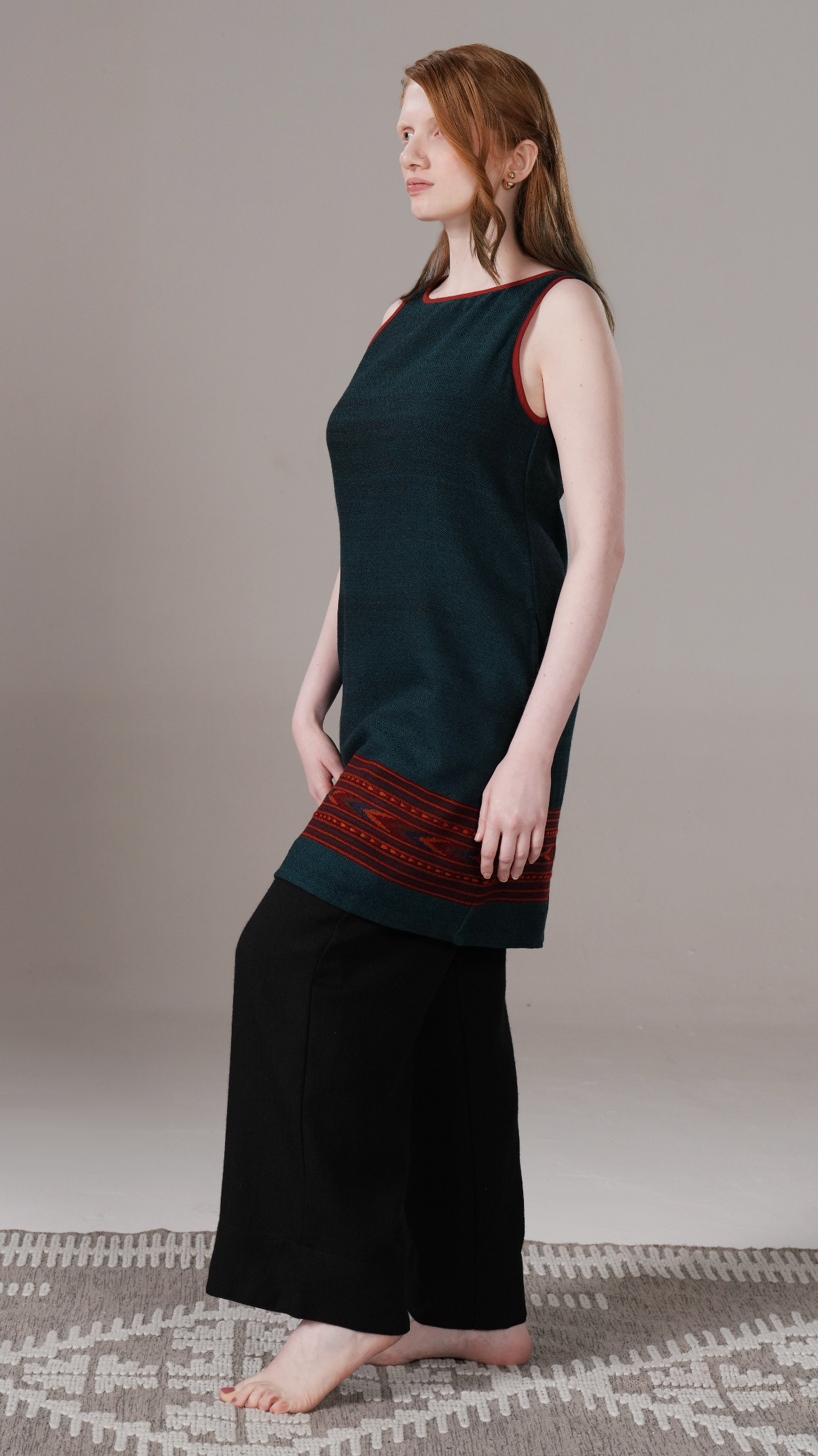 Woman wearing a dark green sleeveless top and black pants on a neutral background