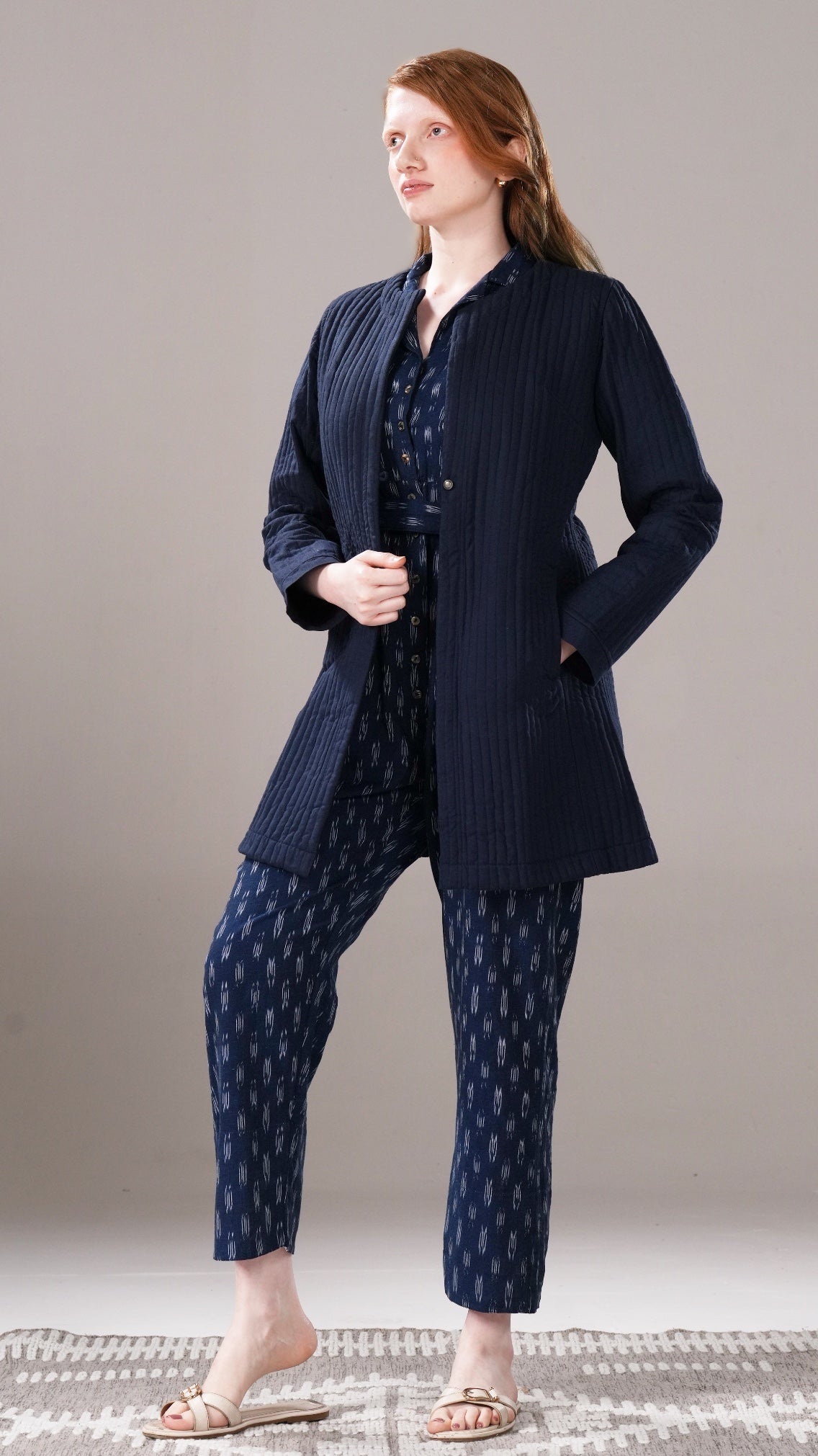 Woman wearing a navy blue outfit with a matching jacket, shirt, and pants on a neutral background.