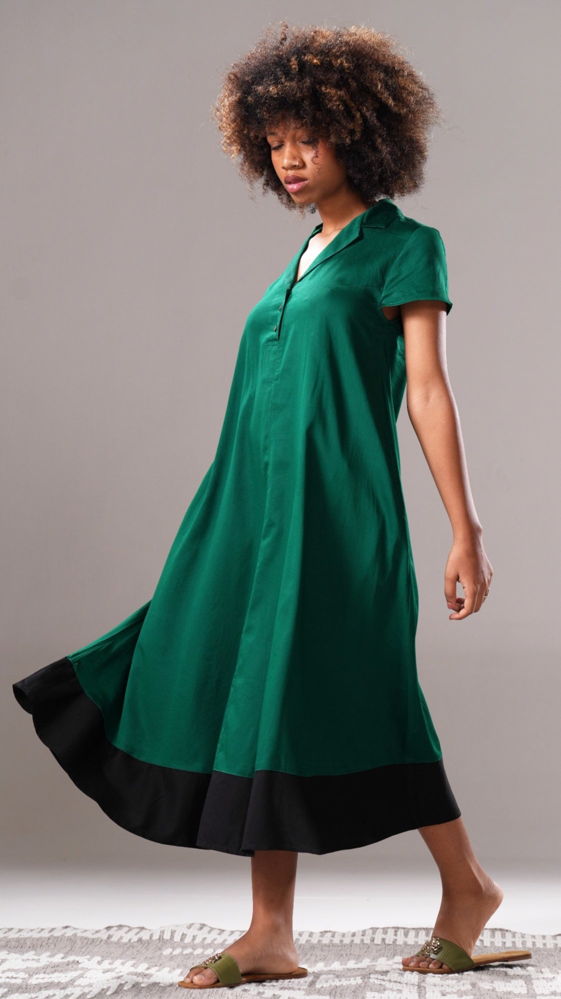 Woman wearing a green dress with black trim on a gray background