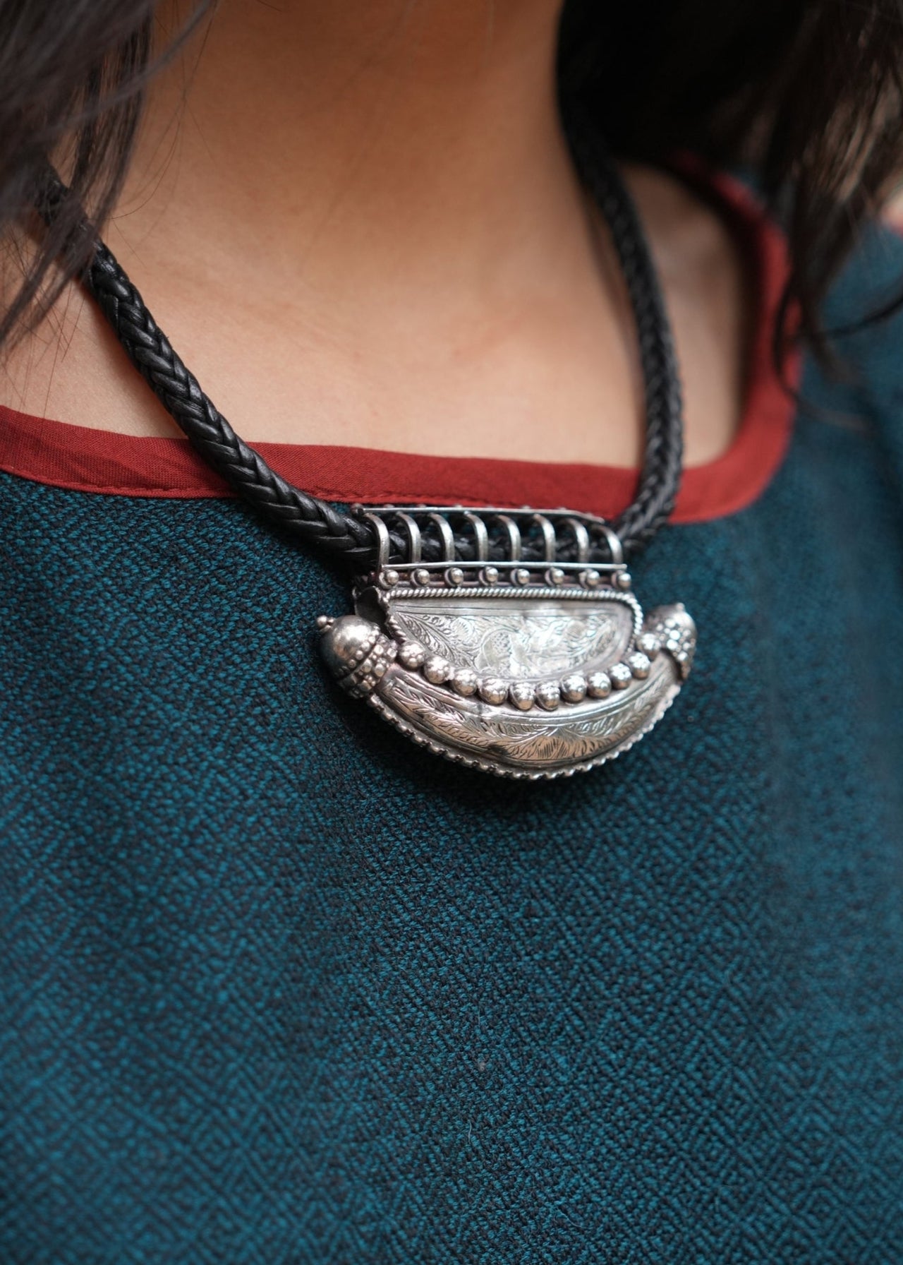 Close-up of a silver necklace with a large pendant on a person wearing a blue garment.