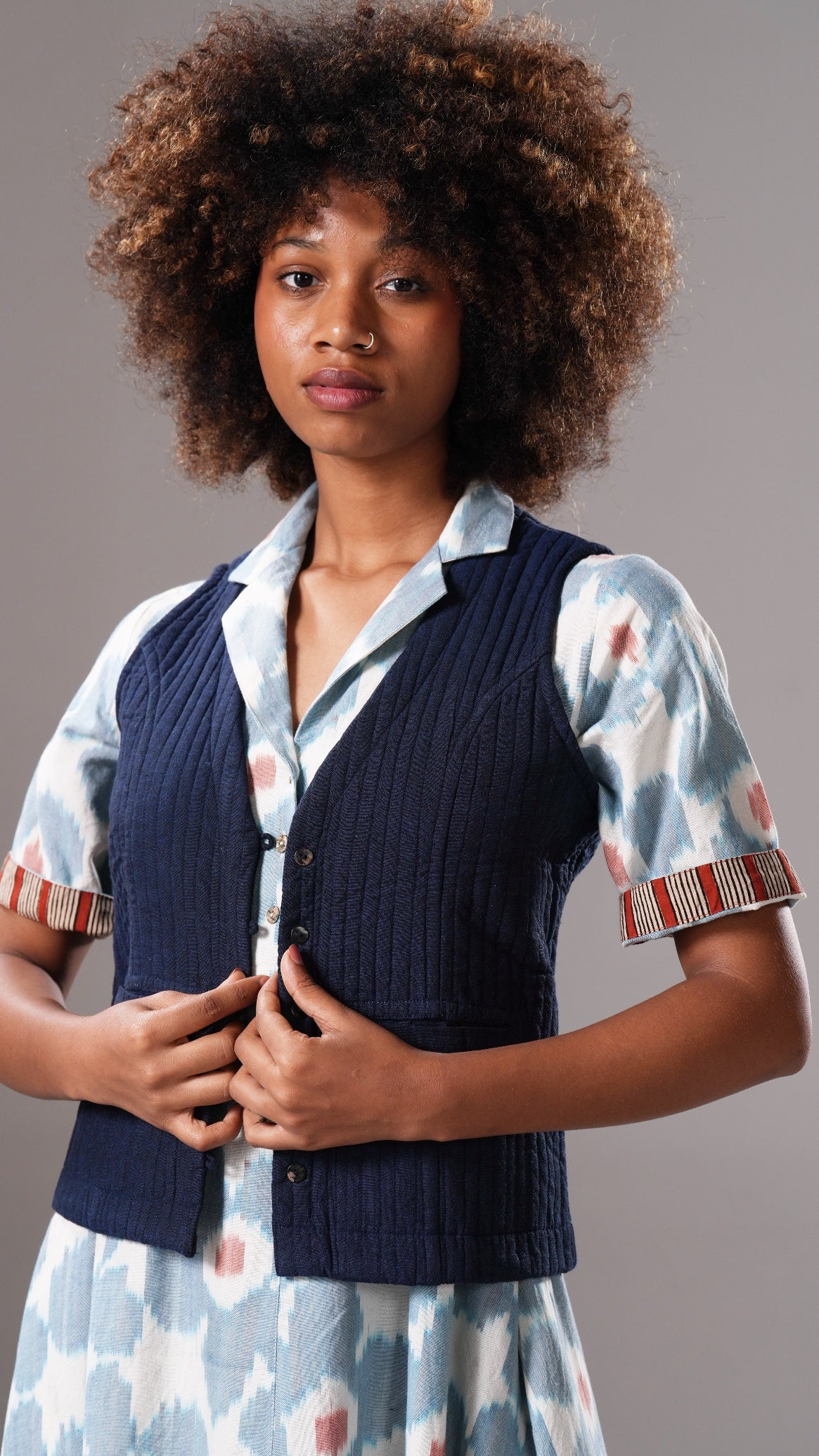 Woman wearing a navy vest over a patterned shirt with a gray background