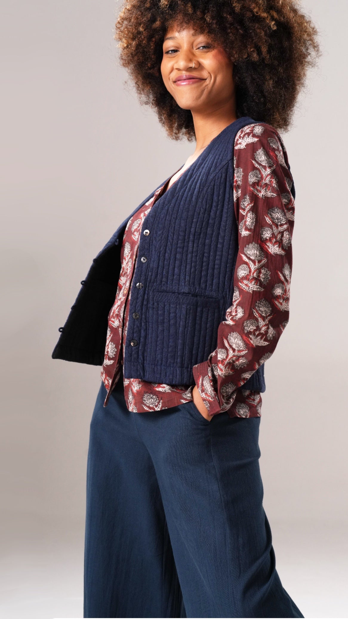 Woman wearing a navy cardigan over a patterned shirt with blue pants on a plain background