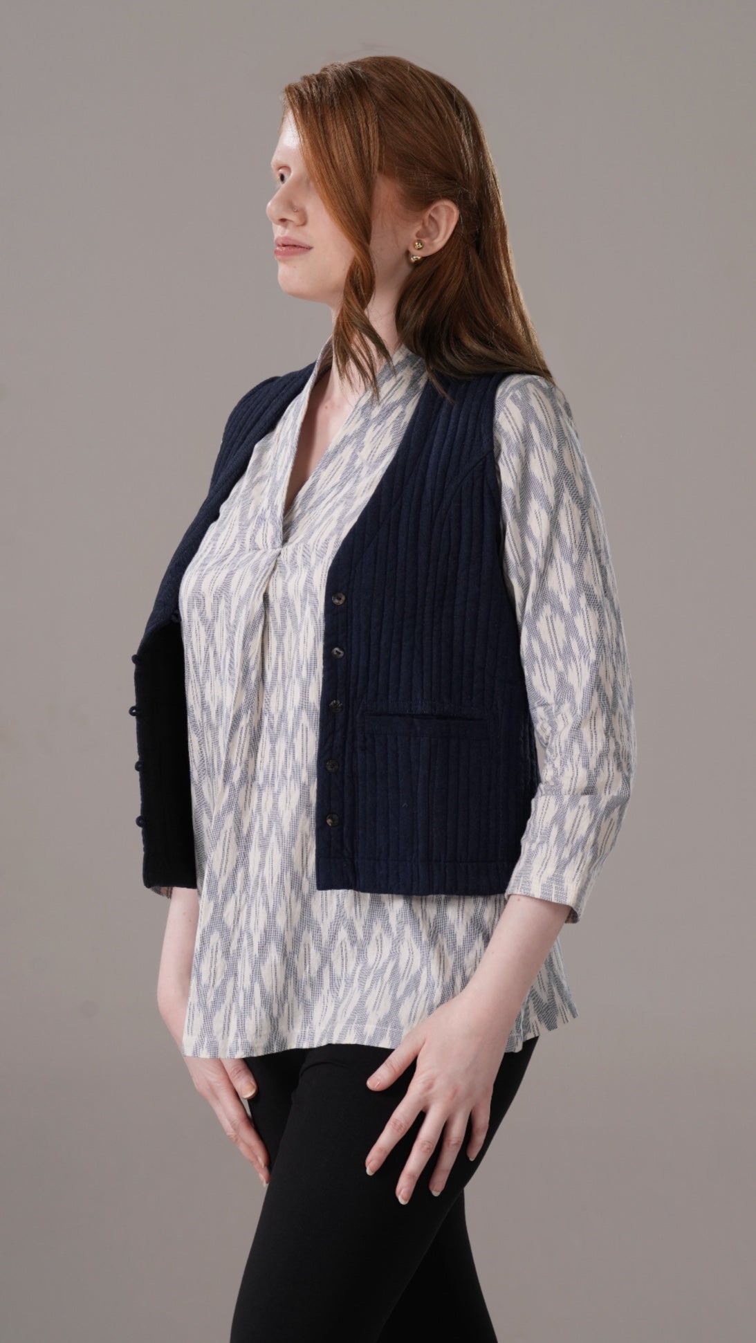 Woman wearing a patterned shirt and navy vest against a plain background
