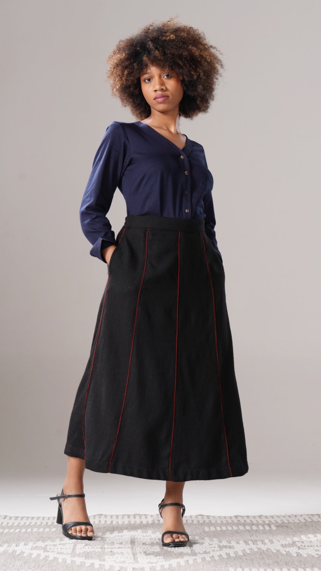 Woman wearing a blue blouse and black skirt with red accents against a gray background