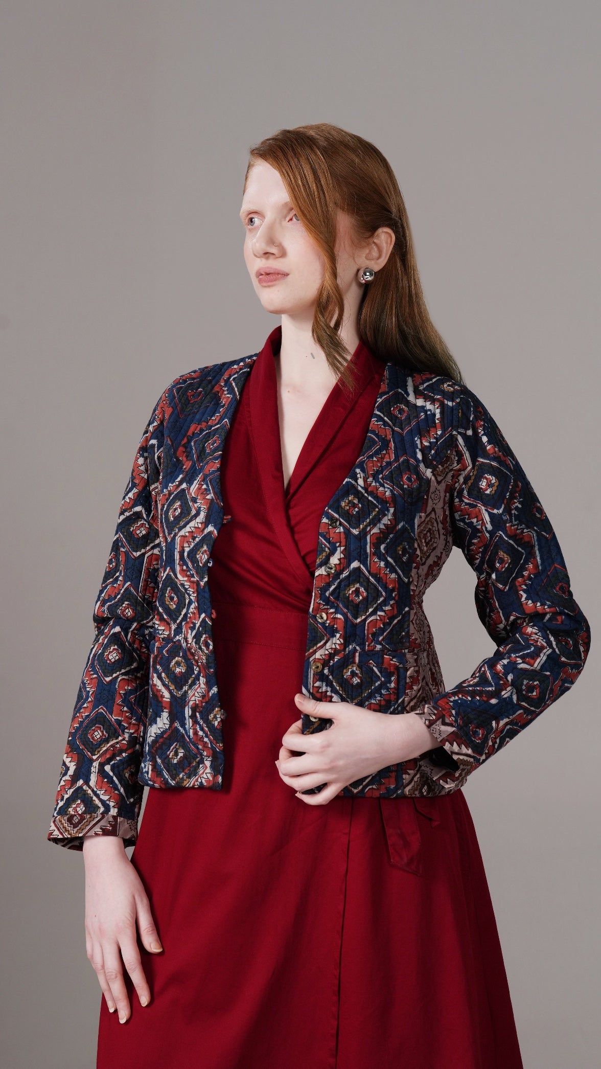 Woman wearing a red dress with an patterned jacket against a gray background
