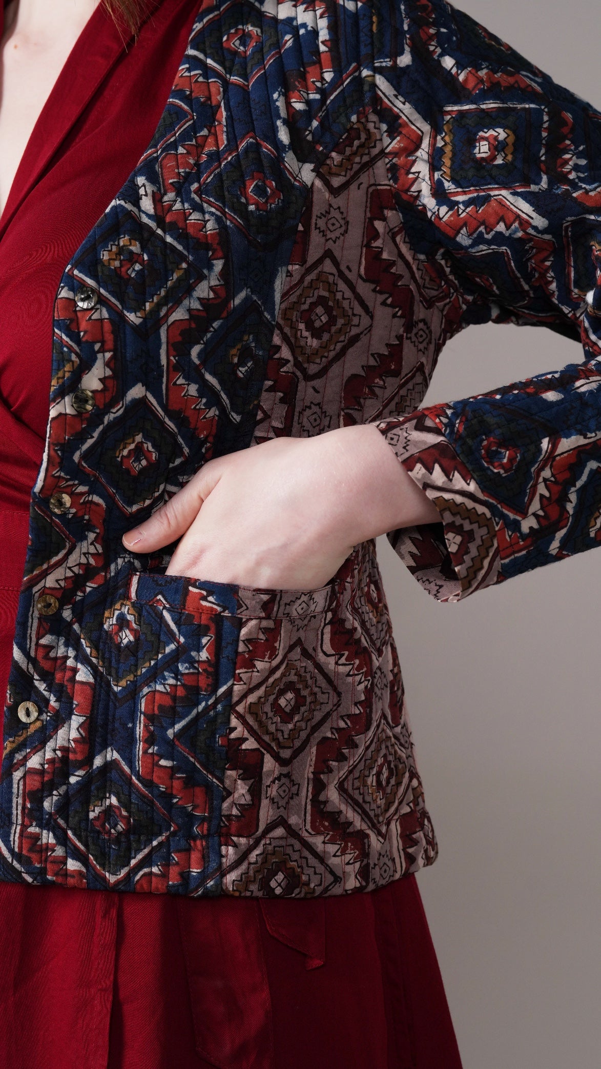 Person wearing a patterned jacket over a red outfit on a neutral background