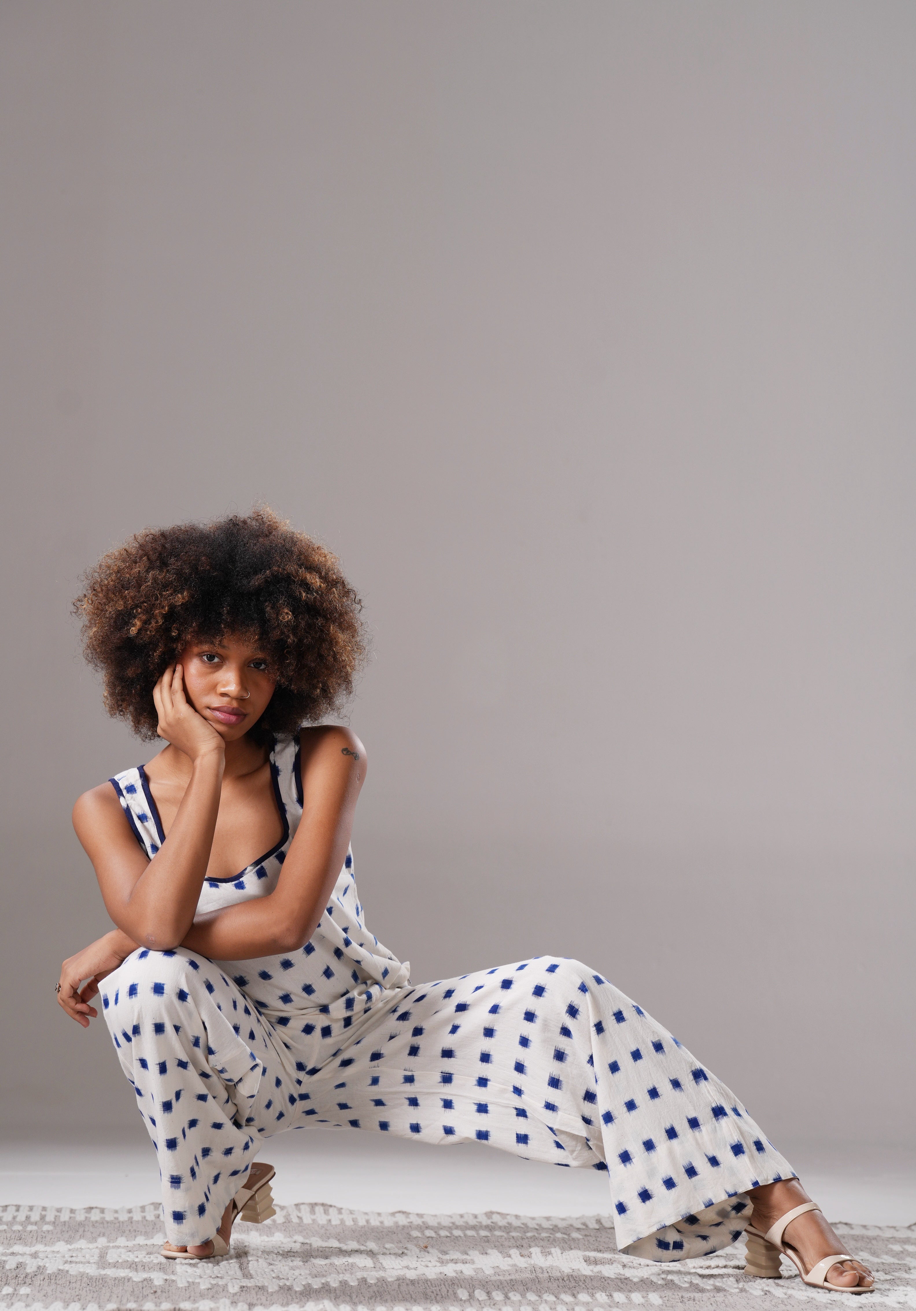 Woman in a polka dot dress sitting on the floor against a plain background