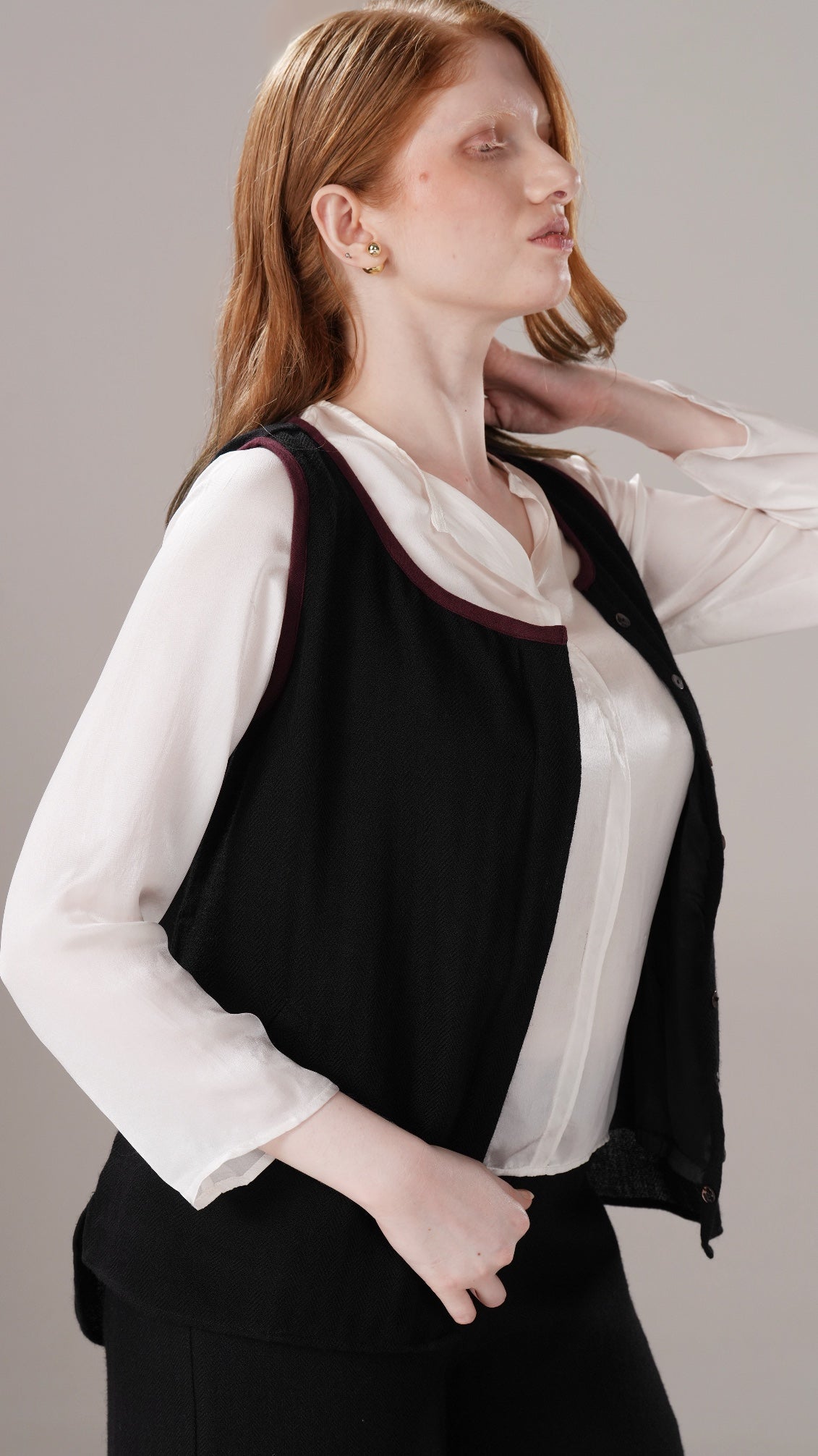 Woman wearing a black vest over a white shirt on a gray background