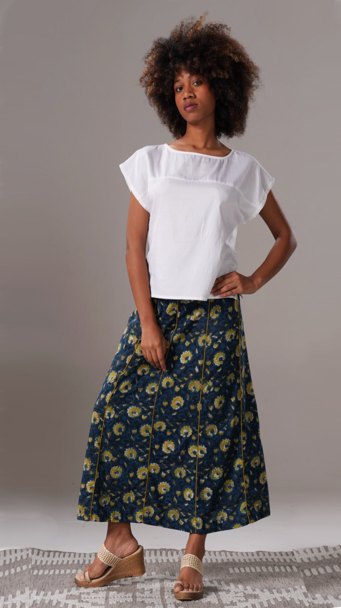 Woman wearing a white top and floral skirt on a plain background