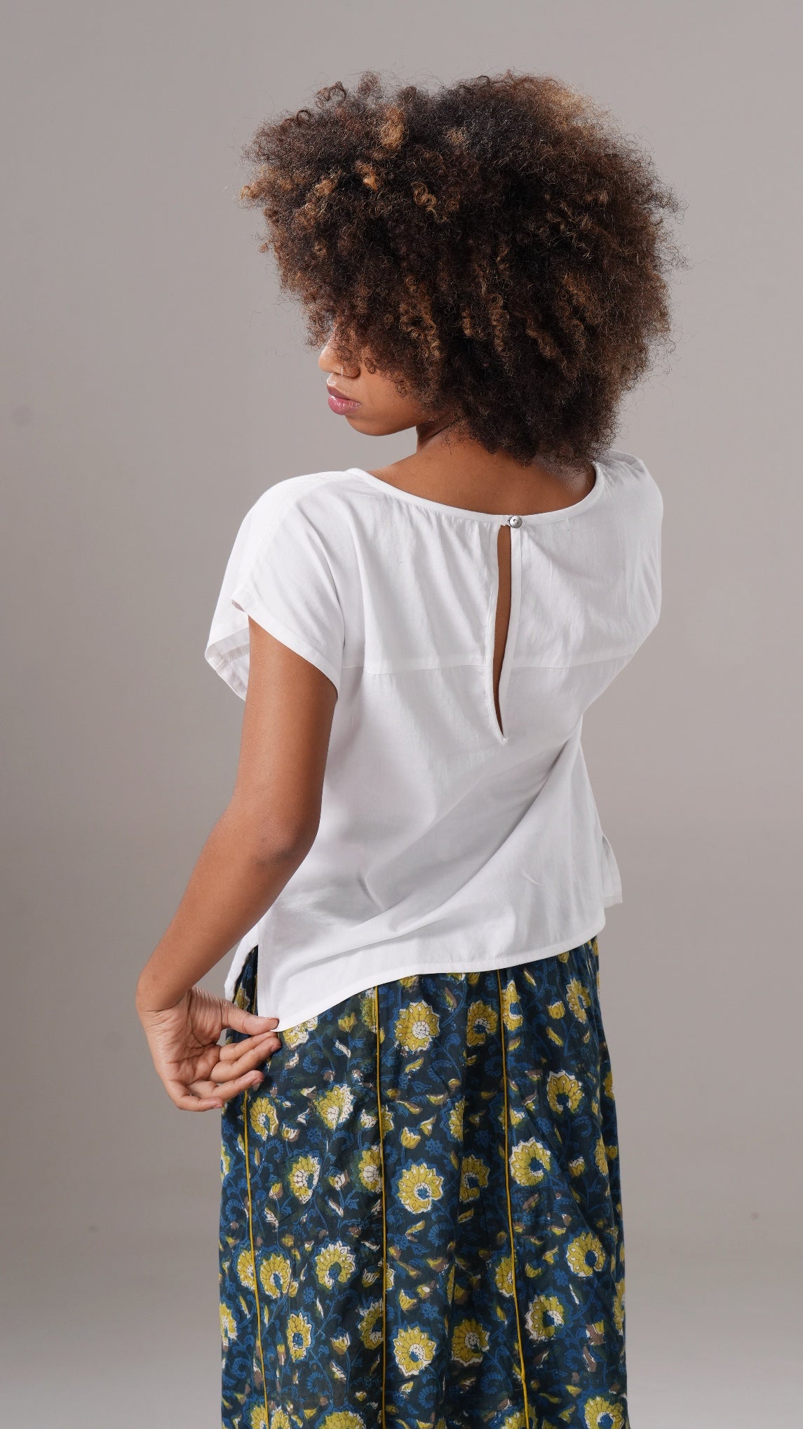 Person wearing a white top with a cutout design and floral pants on a gray background